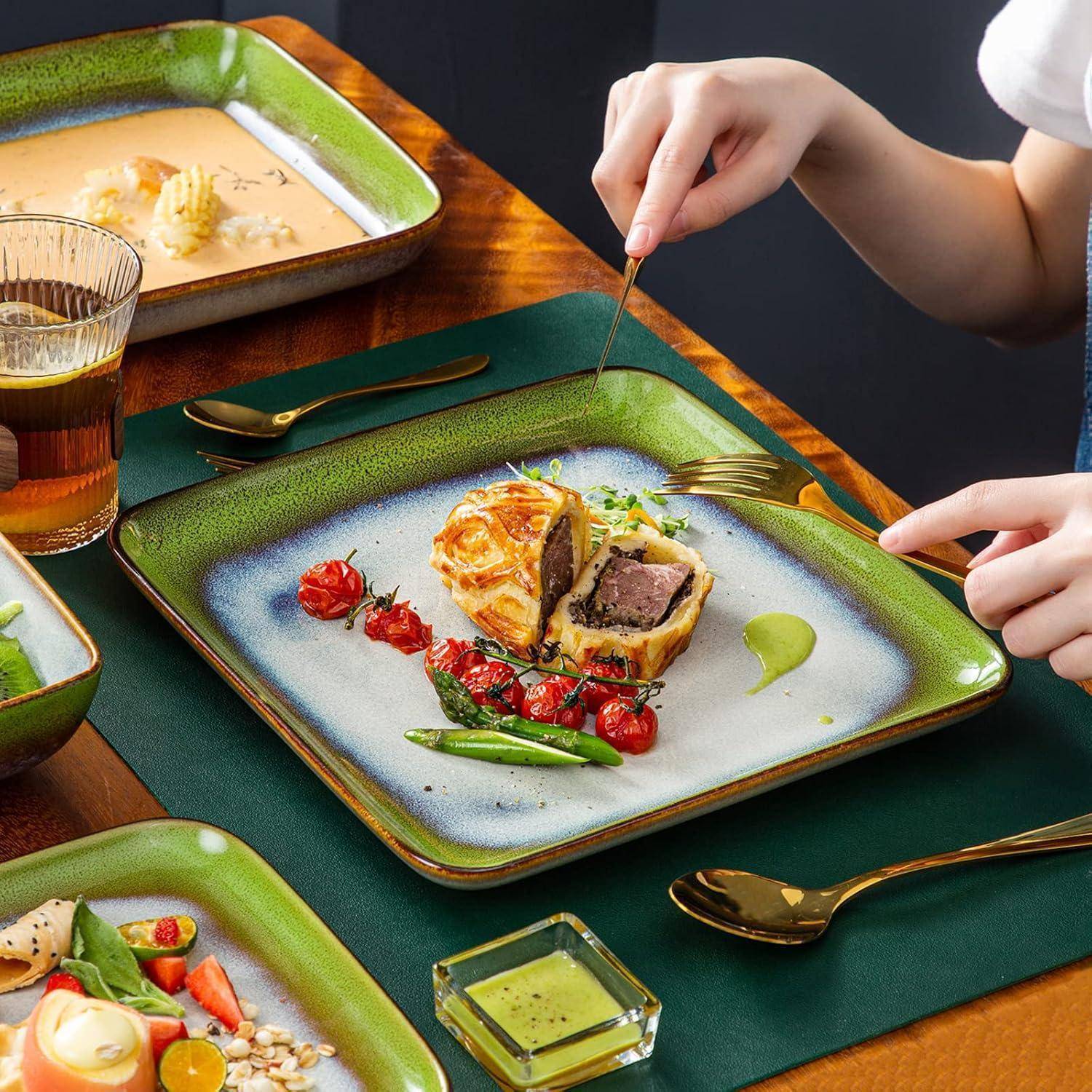 Eine Hand verwendet eine Gabel, um ein Gourmet-Rinderfilet Wellington zu zerteilen, serviert mit Kirschtomaten und Spargel auf einem stilvollen Teller.