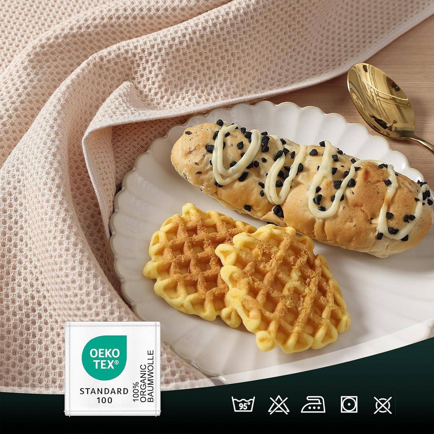 Ein weißer Teller mit zwei Waffeln und einem mit Schokoladenchips beträufelten Gebäck, auf einem Stoffserviette platziert, daneben ein löffelförmiges Blatt.
