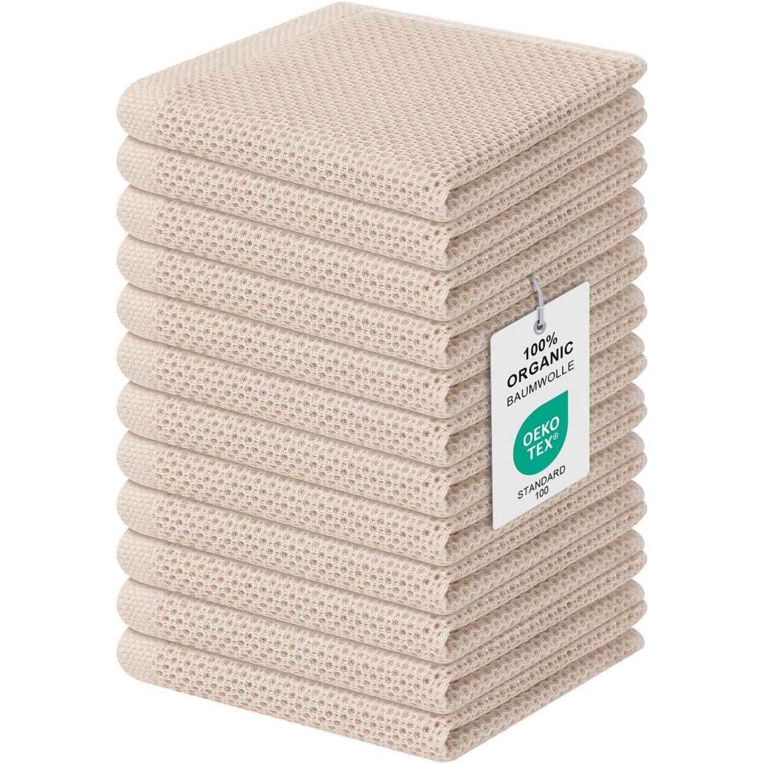 Ein Stapel beiger, gestrickter Waschlappen, die mit dem Etikett '100% Bio-Baumwolle' und dem 'OEKO TEX Standard' Anhänger versehen sind, was auf umweltfreundliches Material hinweist.
