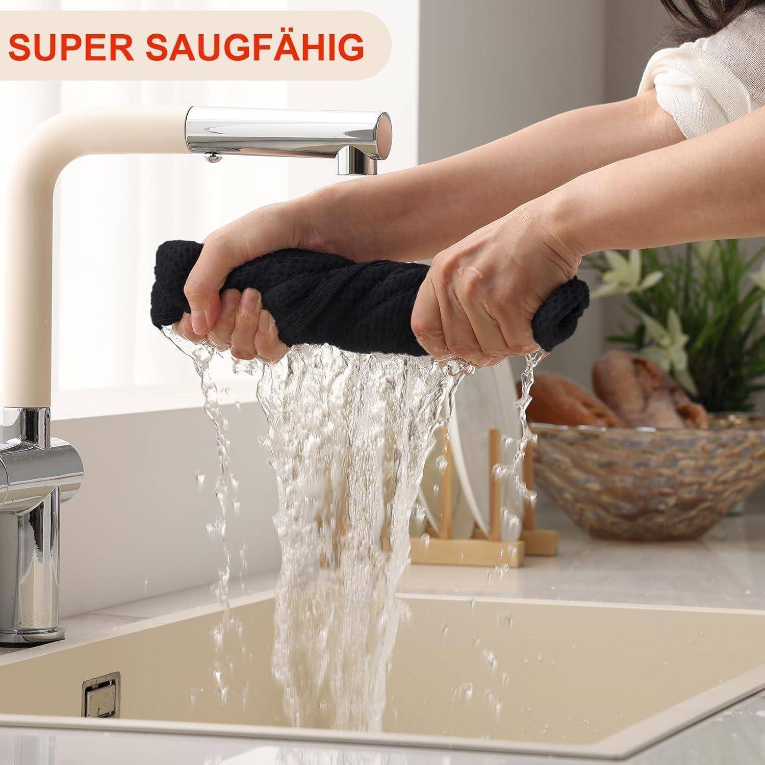 Eine Person, die einen schwarzen Lappen unter einem Küchenarmatur ausdrückt, während Wasser herausläuft und die Absorptionsfähigkeit des Lakens demonstriert.