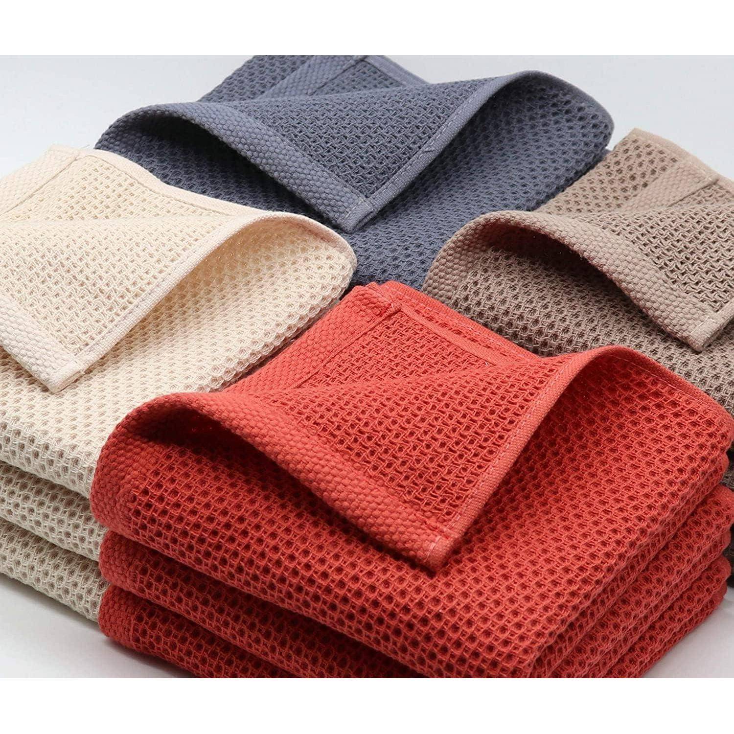 Stapel gefalteter, strukturierter Waschlappen in Grau, Beige, Rot und Creme, die ordentlich angeordnet sind und Details des Gewebes sowie Farbvielfalt zeigen.