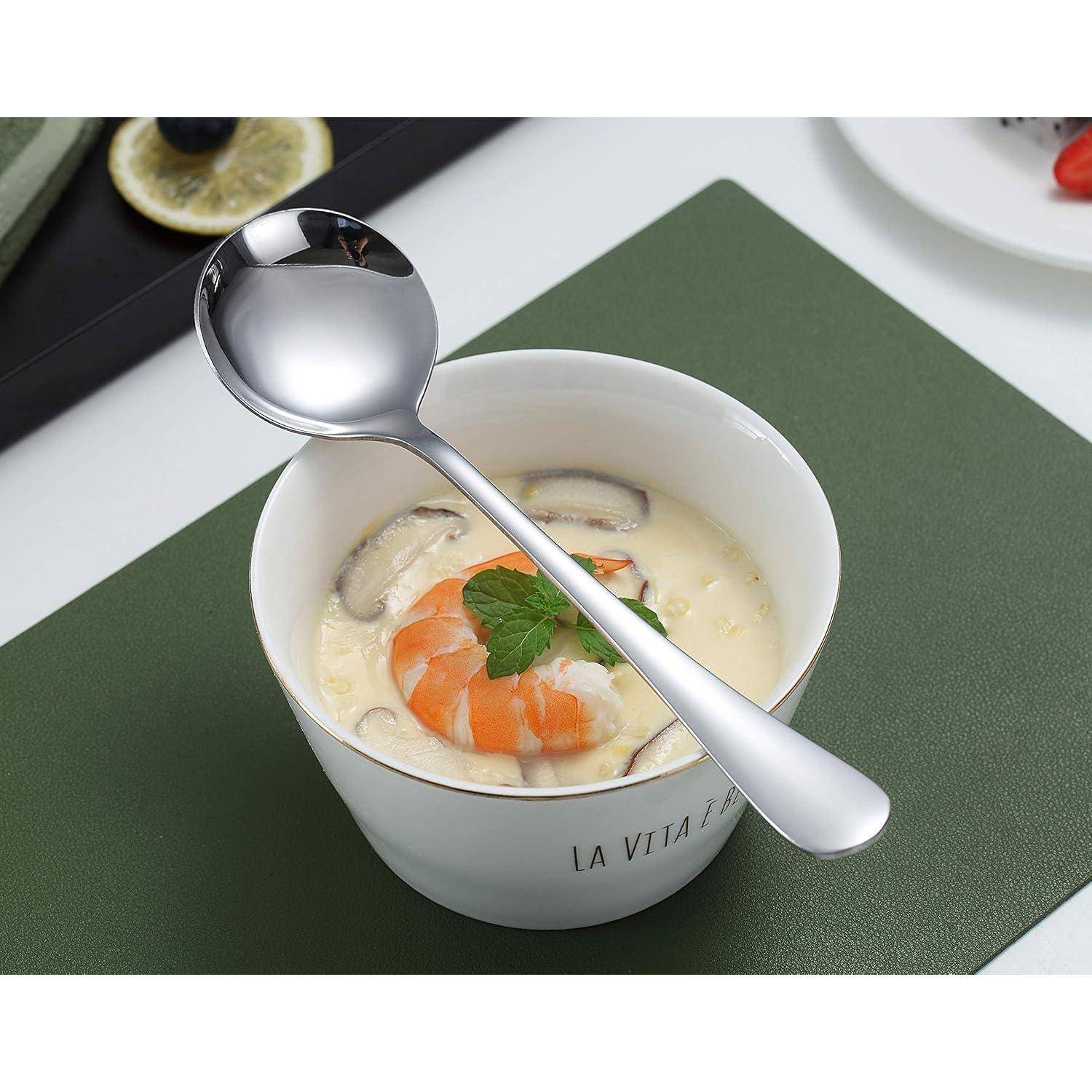 Eine Schüssel cremiger Suppe mit geschnittenen Pilzen, garniert mit Garnelen und Petersilie, neben einem polierten Löffel auf einer grünen Tischdecke.