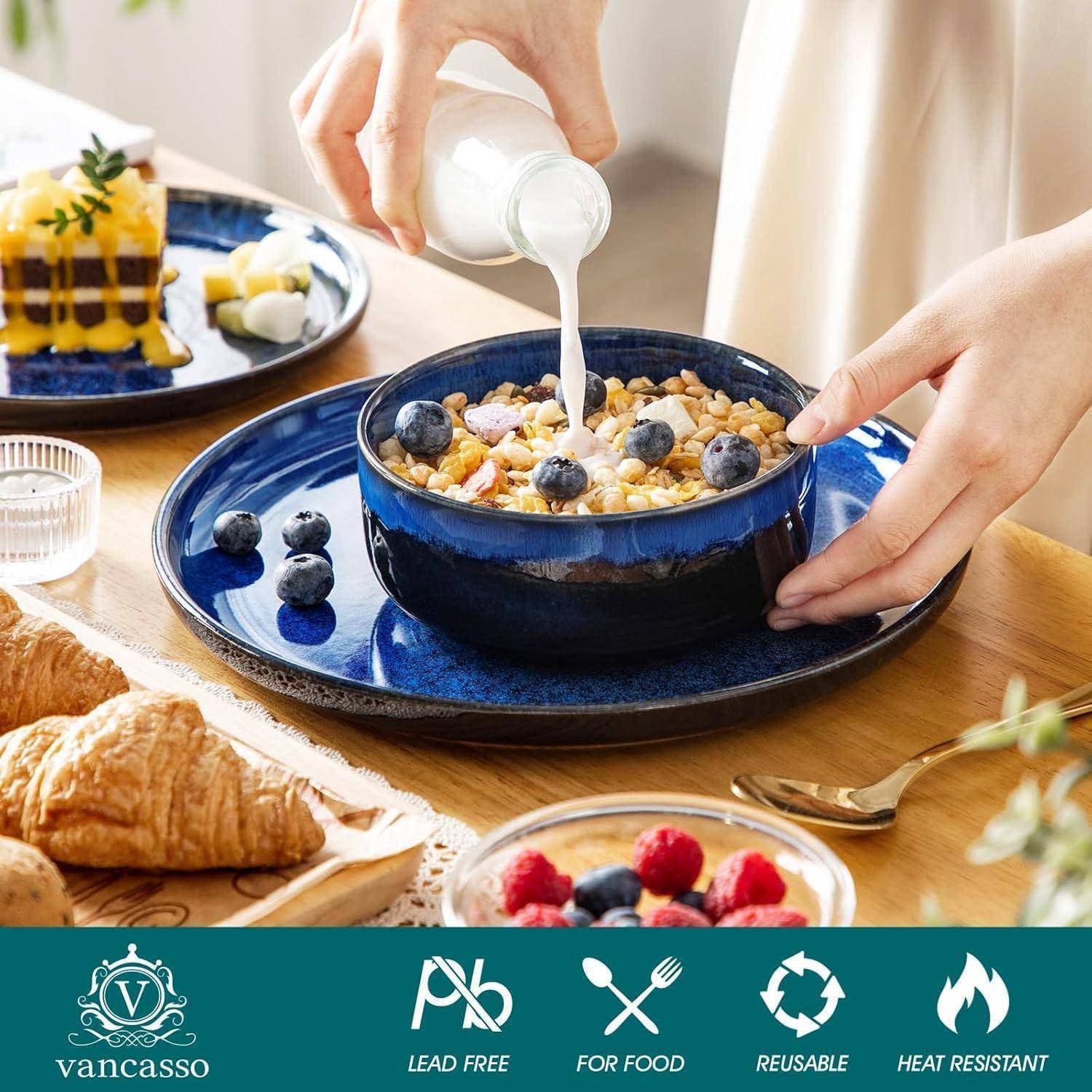 Eine Person gießt Milch in eine Schüssel Müsli, die mit Blaubeeren auf einem blauen Teller bedeckt ist. In der Nähe befinden sich Toast mit Eiern, Beeren und Croissants.