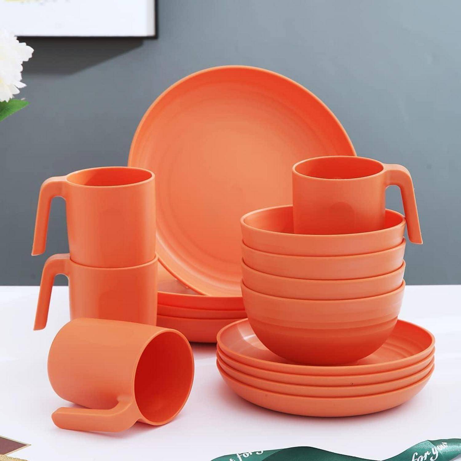 Ein Set aus orangefarbener Geschirrkollektion, einschließlich gestapelter Tassen, Schalen und Teller, die auf einem Tisch platziert sind, mit einem Andeuten eines grünen Platztellers darunter.