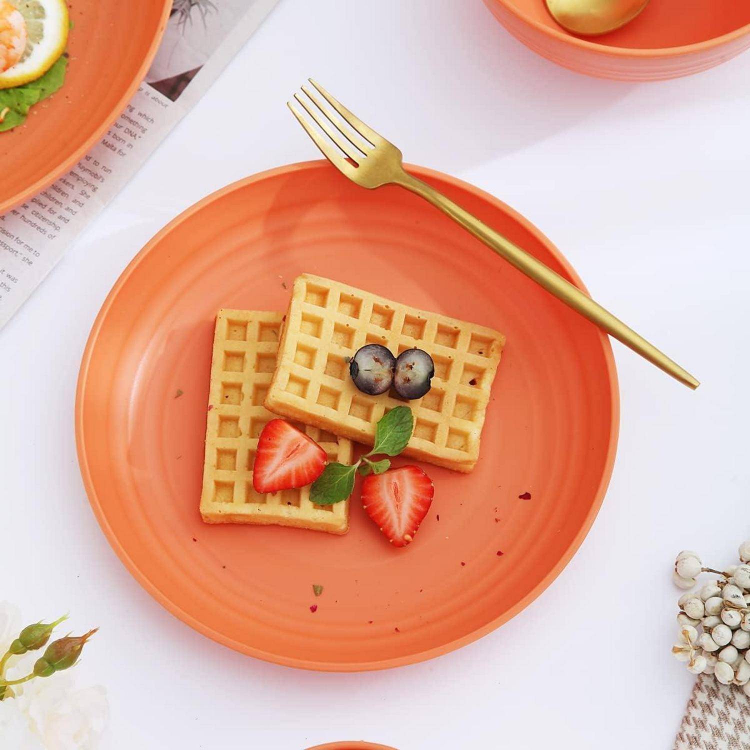 Zwei quadratische Waffeln auf einem orangefarbenen Teller, belegt mit geschnittenen Erdbeeren und Blaubeeren. Eine goldene Gabel liegt daneben auf dem Teller.