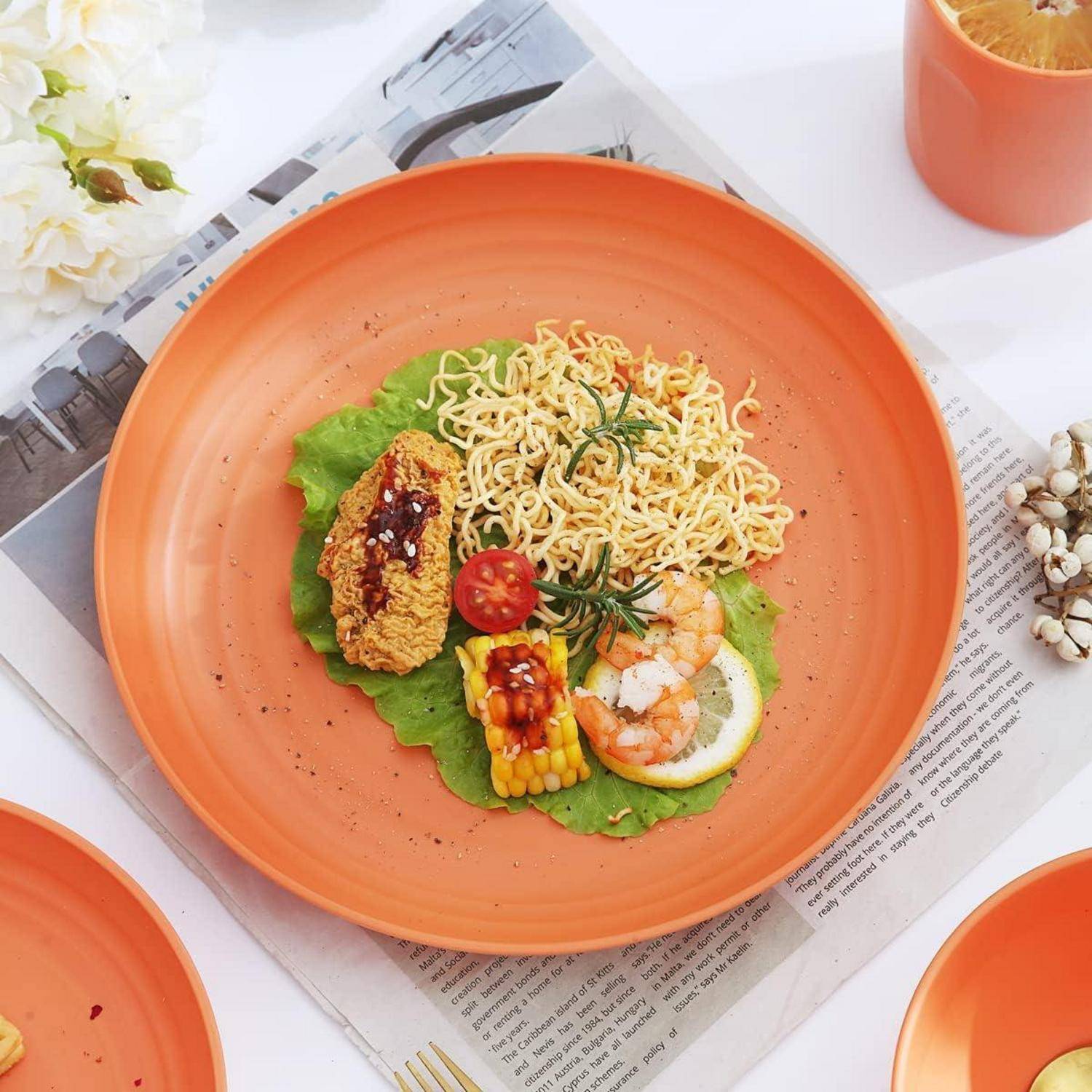 Ein lebendiger orangefarbener Teller mit gegrilltem Mais, Nudeln, Hähnchen, Salat und einer Tomatenscheibe, garniert mit Kräutern und Sauce.