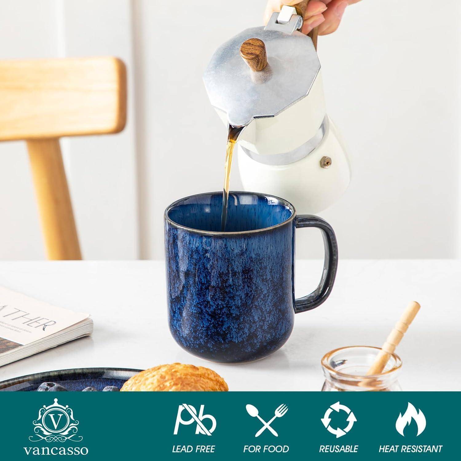Eine blaue Tasse auf einem Tisch wird von einem weißen Metalllkaffeemacher mit Kaffee gefüllt. Auf dem Tisch liegen ein Gebäckstück und ein aufgeschlagenes Buch.