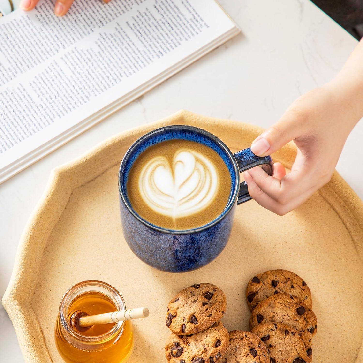 Eine Person bereitet sich darauf vor, einen Latte Art Kaffee, Kekse und Honig auf einem Tablett zu genießen, während ein aufgeschlagenes Buch daneben liegt.