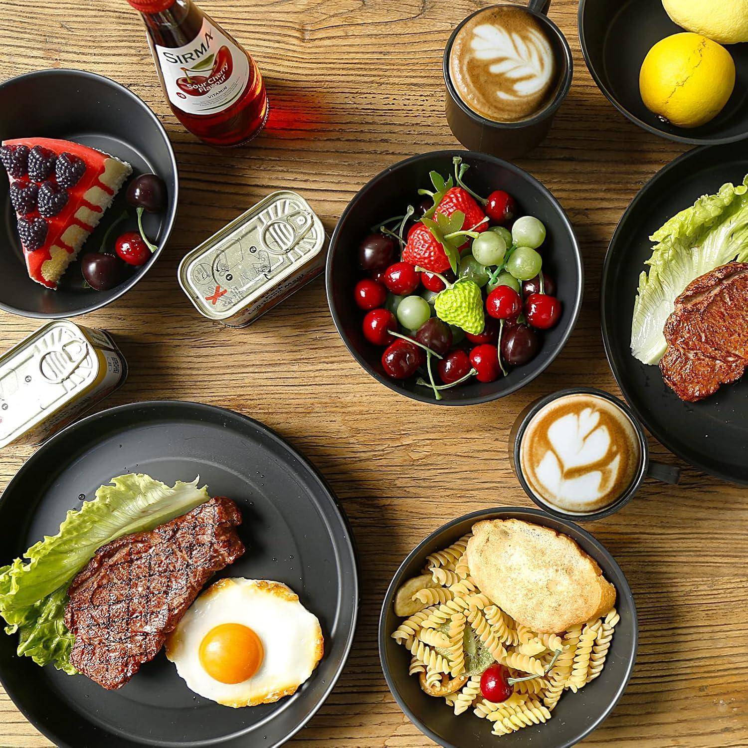 Ein Holztisch mit verschiedenen Speisen: Steak mit Ei und Salat, Dosenfisch, Käsekuchen mit Beeren, frischem Obst, Cappuccino und Saft.