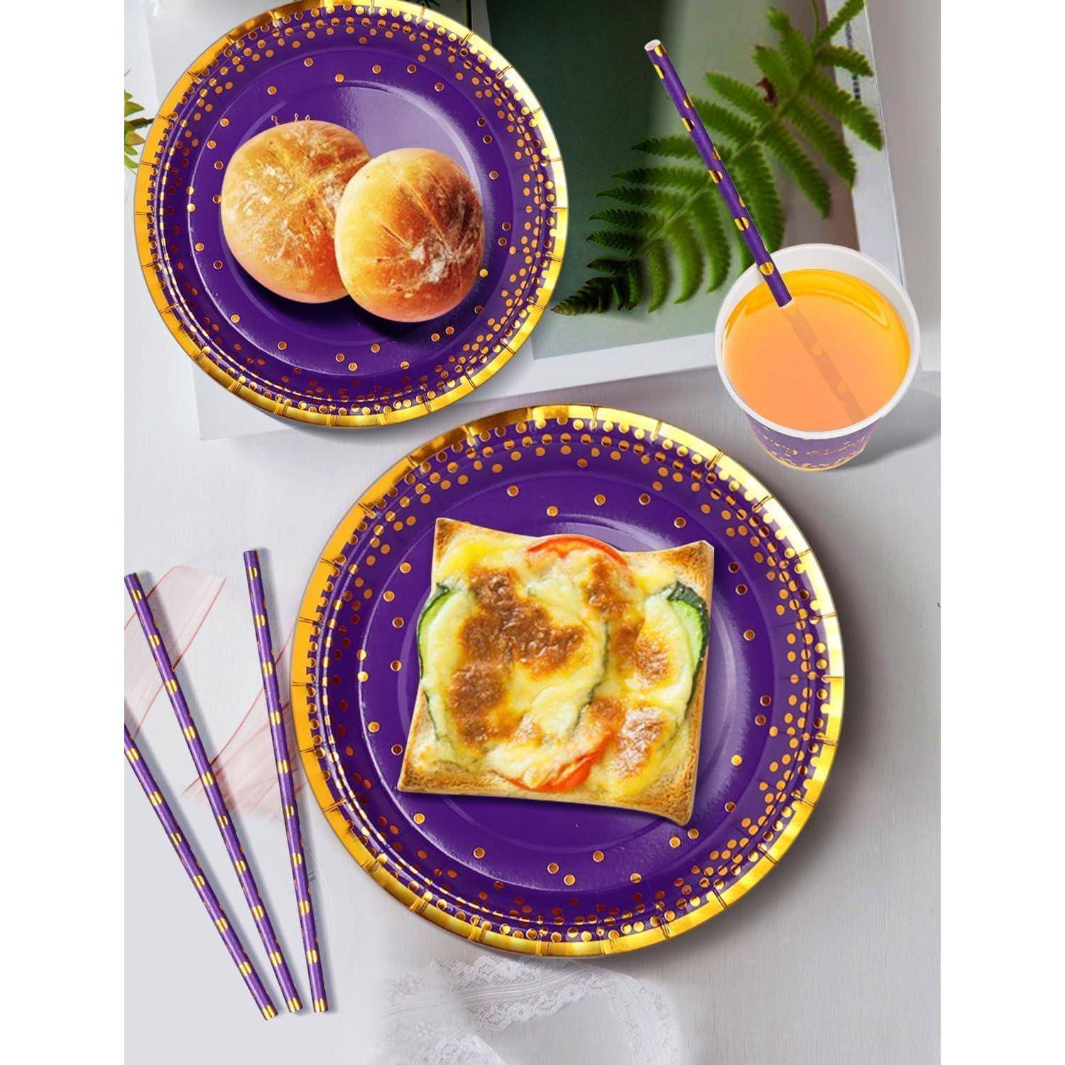 Eine Mahlzeitanordnung mit violetten und goldenen Tellern, auf denen eine Pizzascheibe und Brötchen liegen, daneben ein Glas Orangensaft mit einem Trinkhalm.