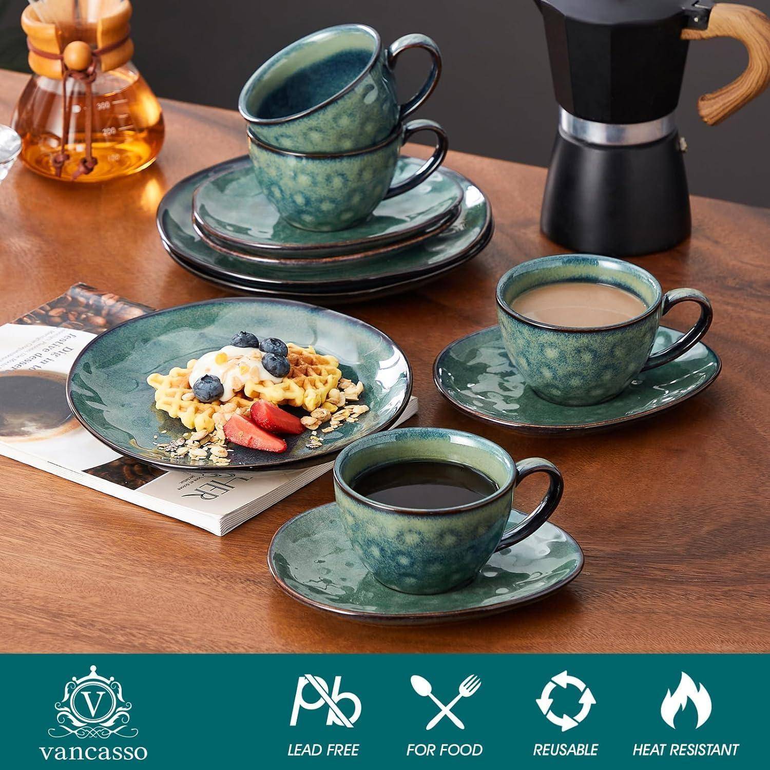 Ein Set aus grünen Keramiktellern, Tassen und Untertassen mit Waffeln, Beeren und Kaffee, auf einem Holztisch neben einem Mokkakocher.