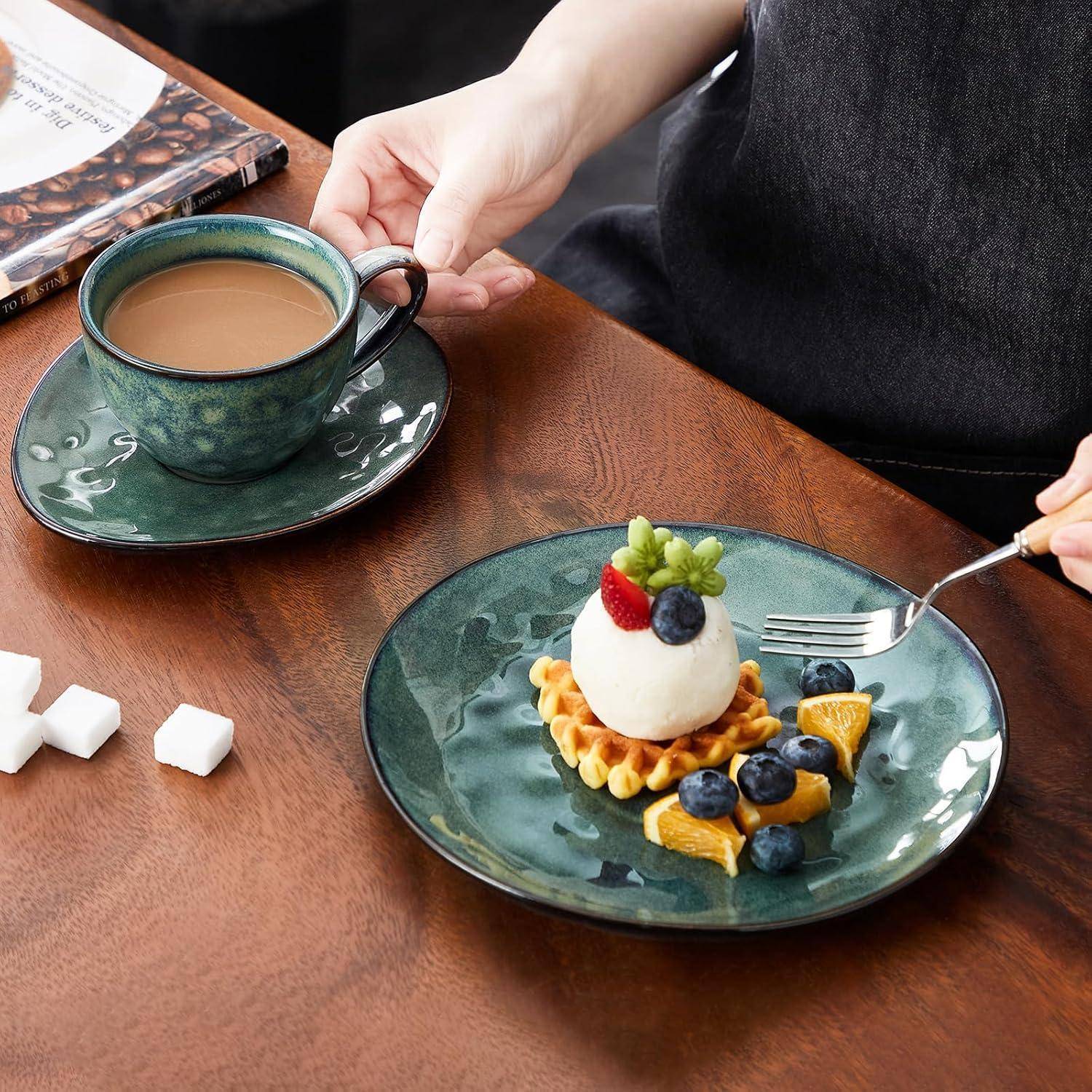 Eine türkisfarbene Kaffeetasse neben einem Dessertteller mit einer Fruchttorte, Blaubeeren und Orangenscheiben. Eine Hand hält einen Löffel neben dem Teller.