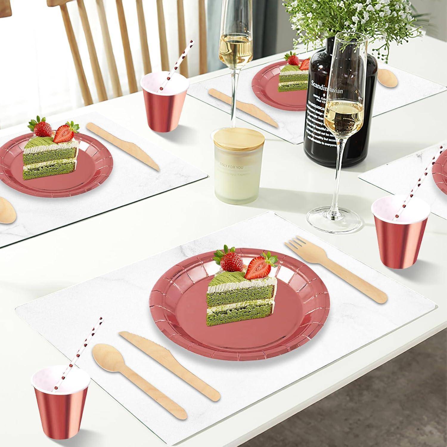 Eine Tischdecke mit drei rosa Tellern, auf denen jeweils ein Stück grüner Kuchen mit Erdbeeren liegt. Holzbesteck, Tassen und Weingläser sind ebenfalls angeordnet.