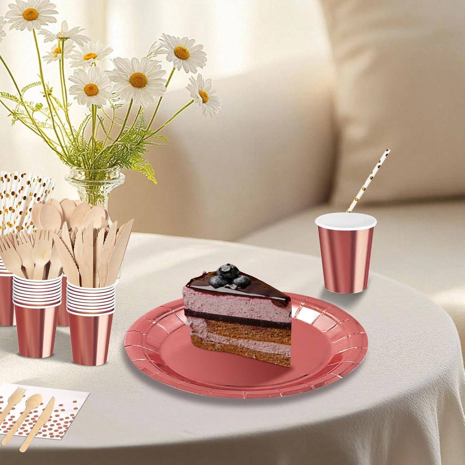 Ein dekorierter Tisch mit einem Stück Kuchen auf einem roten Teller, einer Tasse mit einem Strohhalm und einer Vase mit Gänseblümchen. Holzbesteck ist daneben angeordnet.