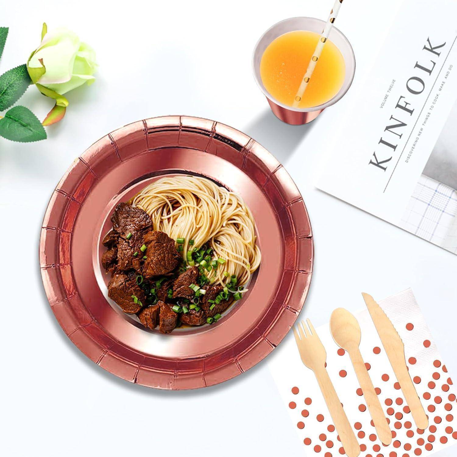 Eine Schüssel mit Nudeln, Rindfleisch und Gemüse auf einem Tisch, begleitet von Orangensaft, einer Rose, einer Zeitschrift und Holzbesteck.