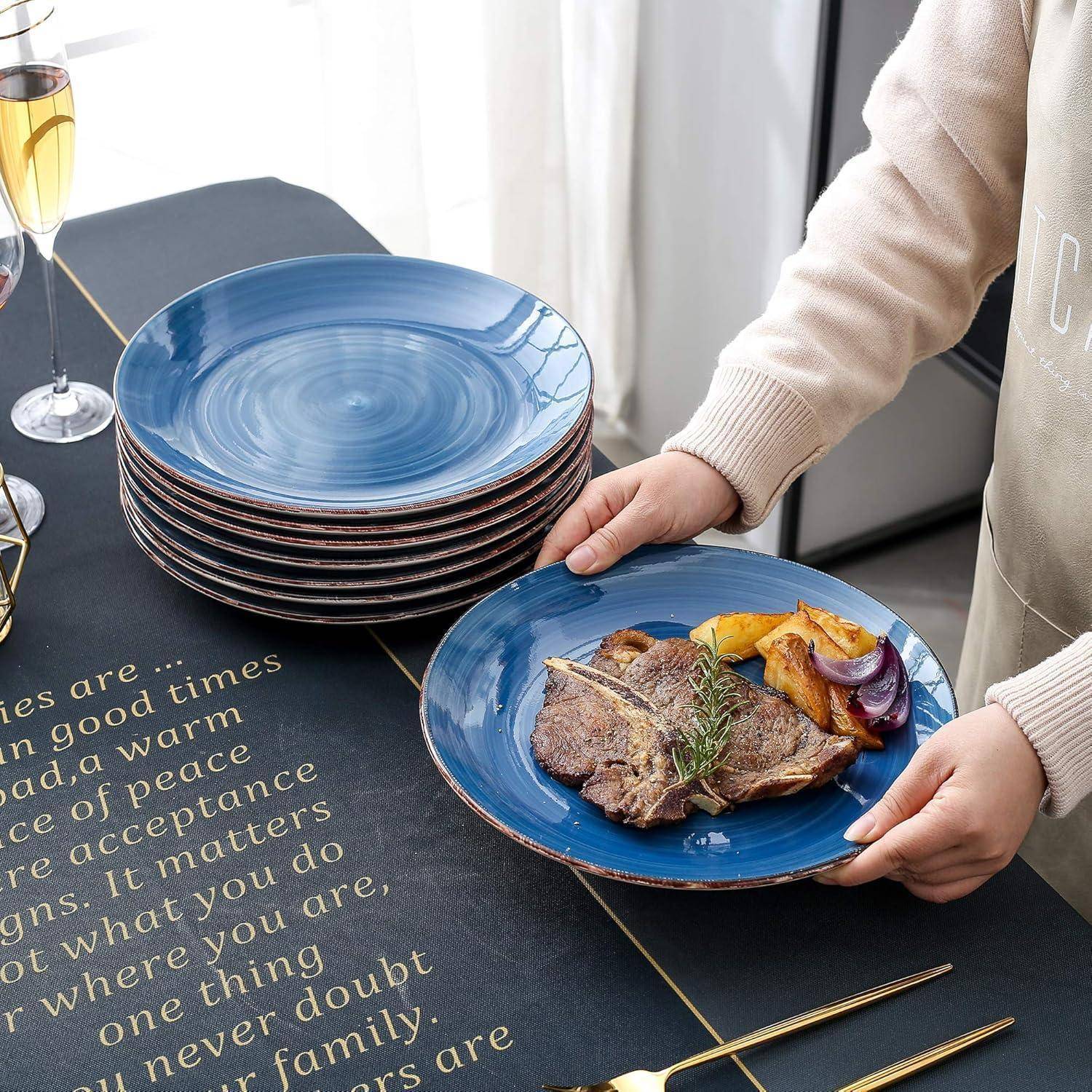 Eine Person legt ein Steak mit Gemüse auf einen blauen Teller. In der Nähe steht ein Stapel ähnlicher Teller, zwei Champagnergläser und Text über Auswahlmöglichkeiten.