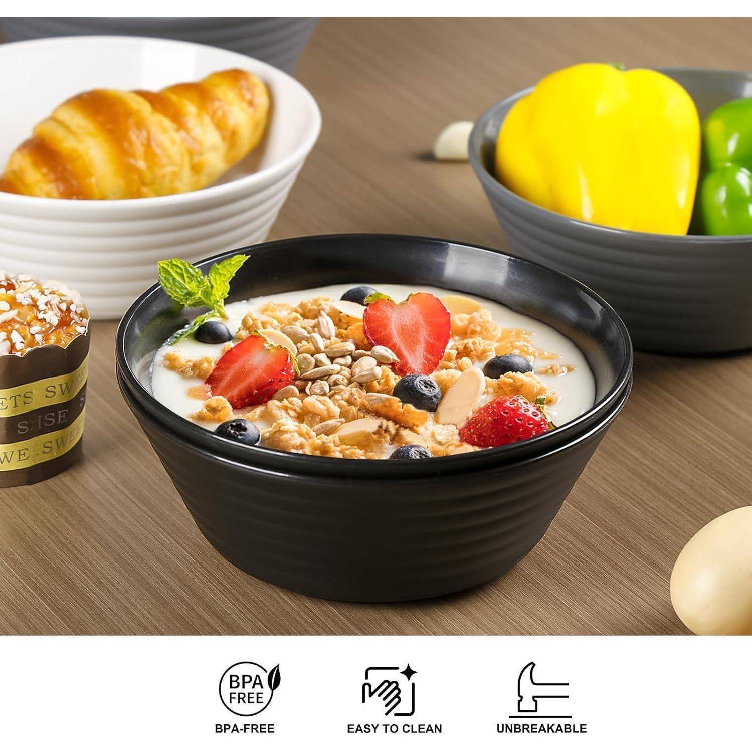 Eine schwarze Schüssel mit Joghurt, bestreut mit Granola, Erdbeeren und Blaubeeren steht auf einem Holztisch. In der Nähe liegen ein Croissant und eine Paprika.