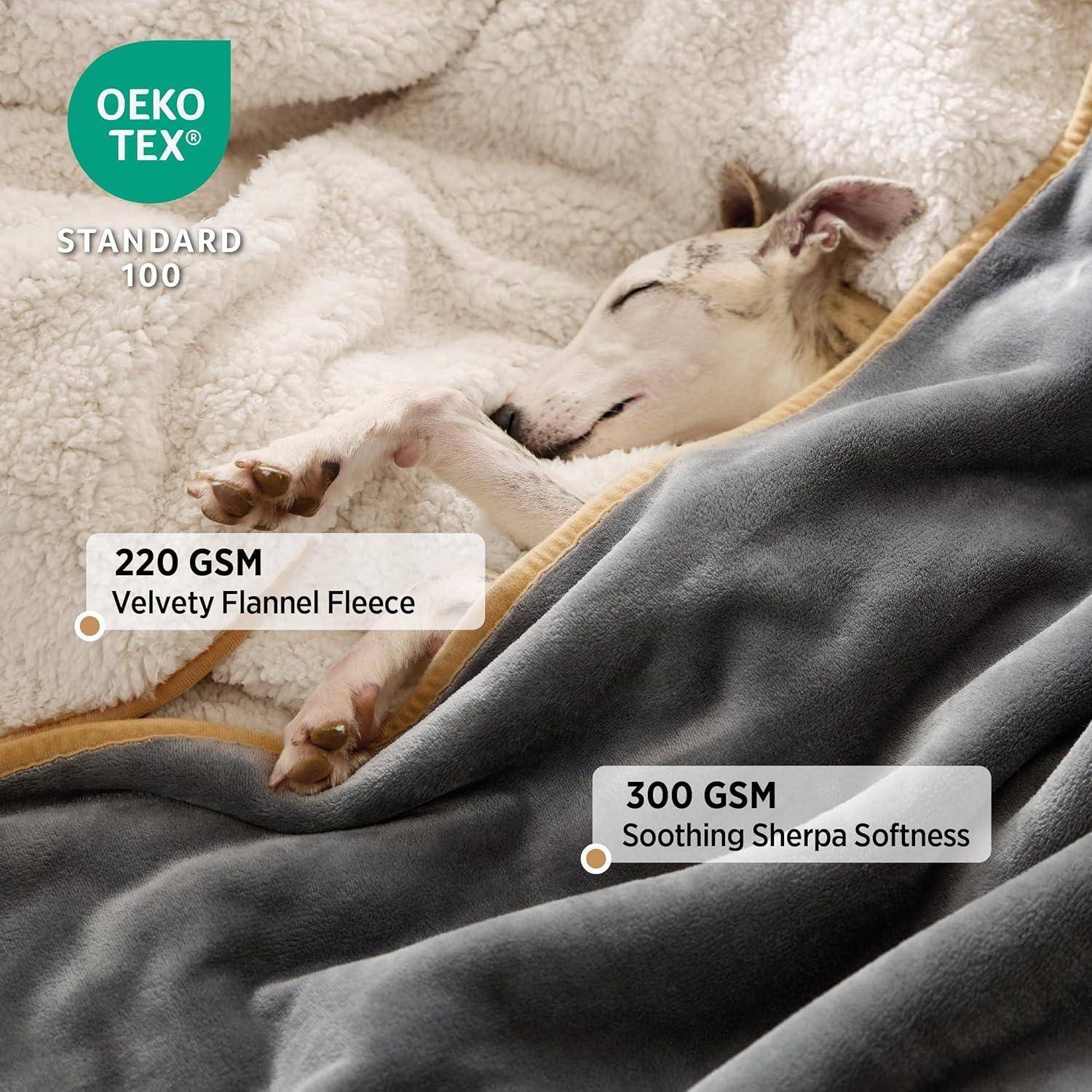 Ein Hund schläft gemütlich unter grauen und cremefarbenen Decken. Das Bild hebt '220 GSM samtig-weiche Flanellfleece' und '300 GSM beruhigende Sherpa-Weichheit' hervor.