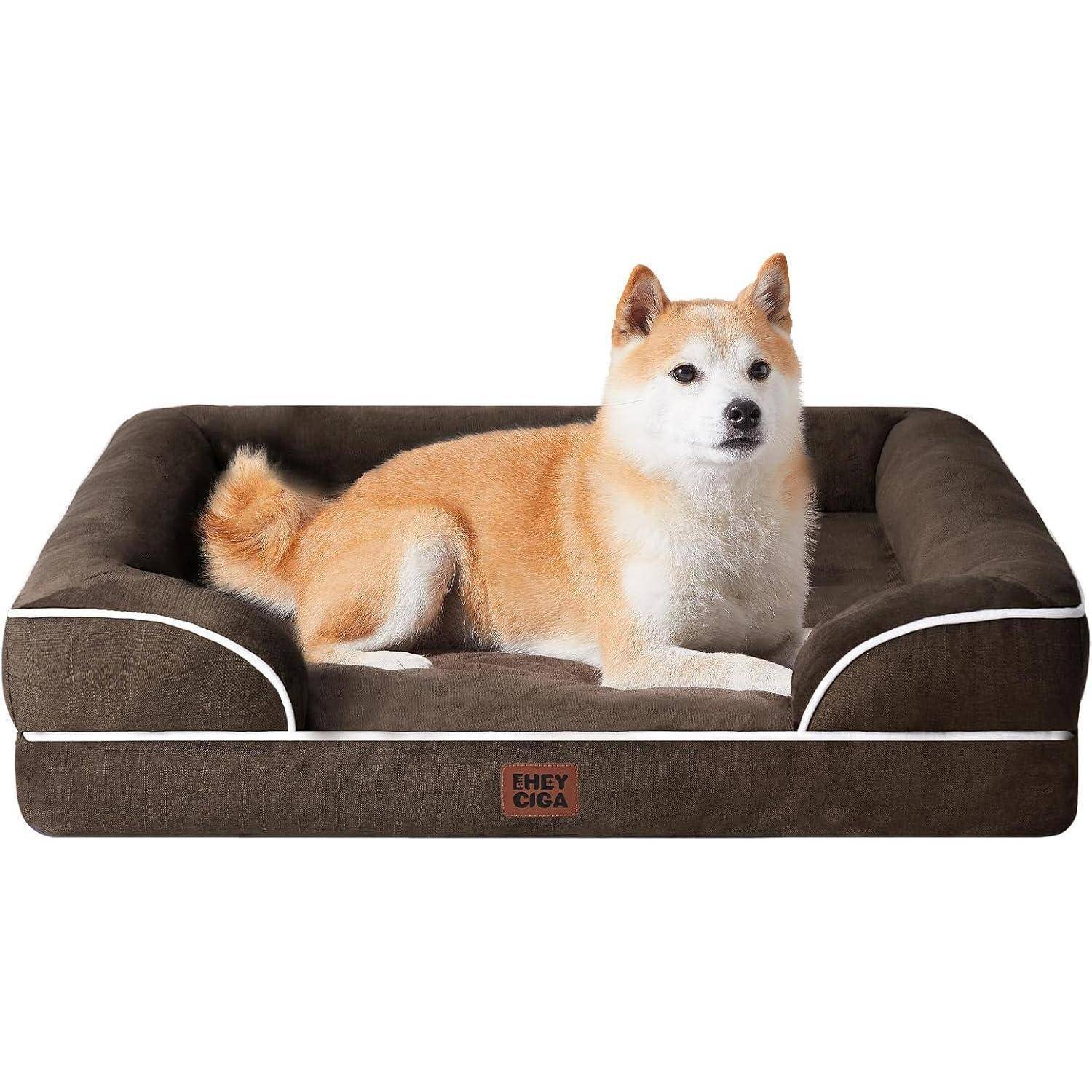 Ein beige-weißer Hund sitzt auf einem plüschigen, braunen rechteckigen Hundebett mit weißer Einfassung, zentral positioniert, und blickt in Richtung Kamera.