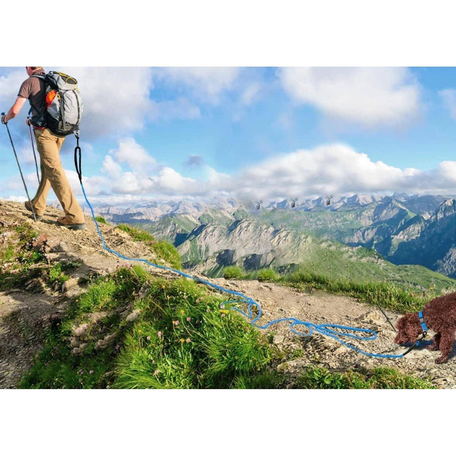 Ein Wanderer mit einem Rucksack erklimmt einen grasigen Bergpfad mit Hilfe eines Seils, mit weiten Ausblicken auf entfernte Berge unter einem teilweise bewölkten Himmel.