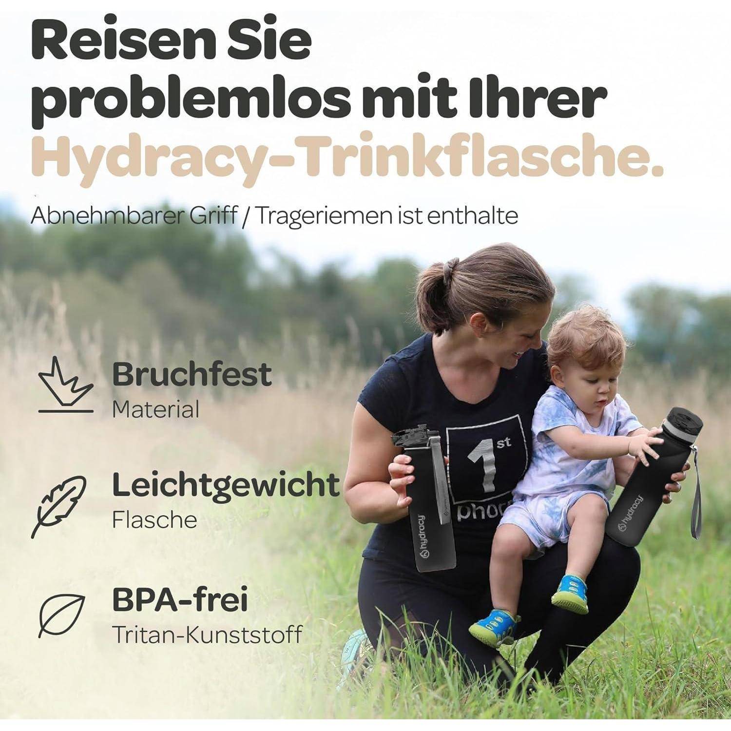 Eine Frau sitzt auf Gras und hält ein Kind und eine Wasserflasche mit der Aufschrift 