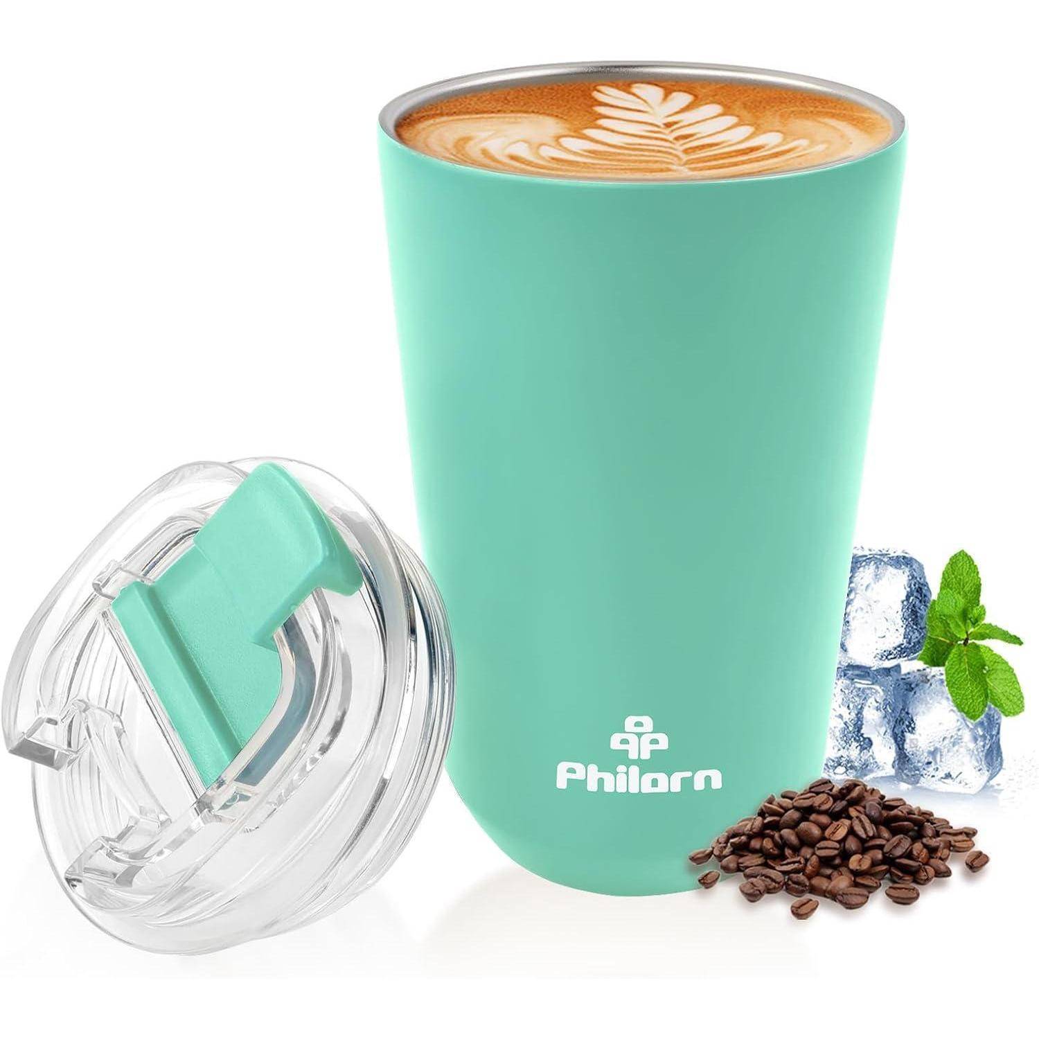 Ein türkisfarbener isolierter Thermobecher mit einem Latte-Art-Design auf der Oberseite, ein offener Deckel daneben, umgeben von Kaffeebohnen, Eiswürfeln und Minzblättern.