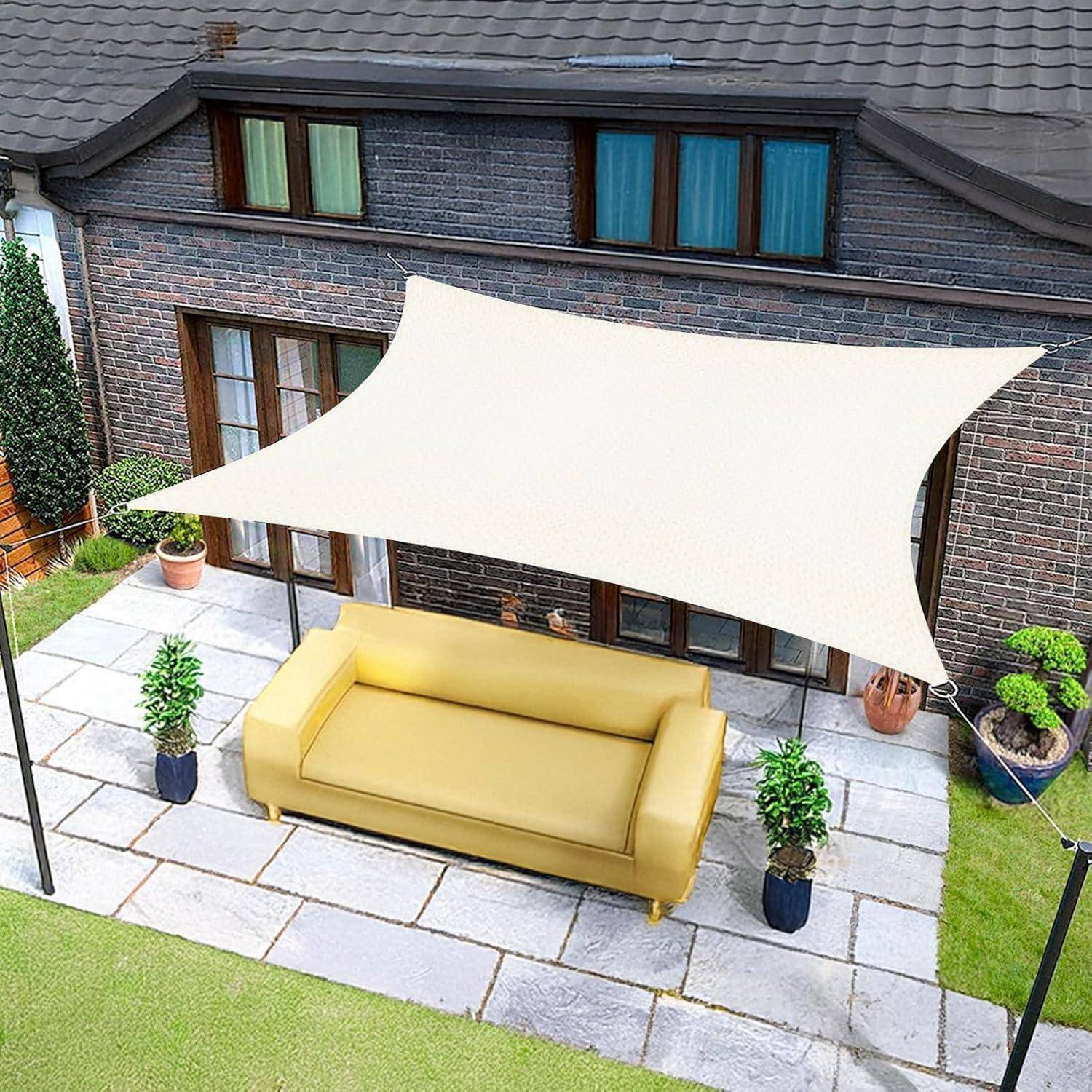 Ein gelbes Outdoor-Sofa steht auf einer Terrasse unter einem großen weißen Sonnensegel, mit Topfpflanzen daneben und einem Backsteinhaus im Hintergrund.