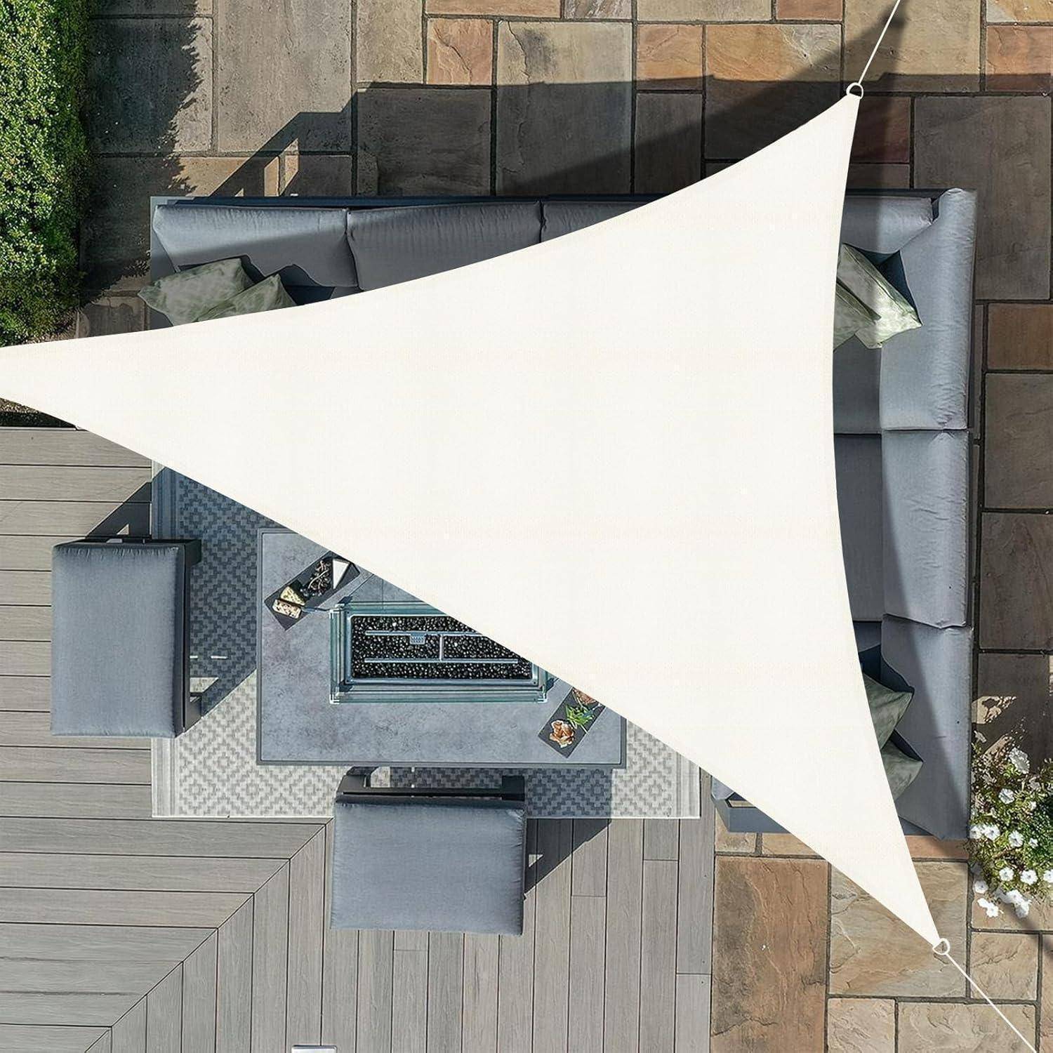 Luftaufnahme einer Terrasse mit grauen Sitzmöbeln und einer Feuerstelle, die von einem großen weißen dreieckigen Sonnensegel beschattet wird, umgeben von Pflanzen und Steinfliesen.