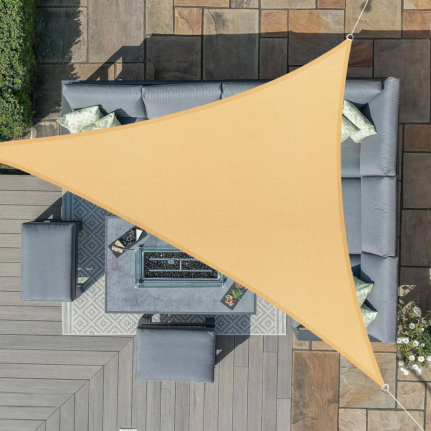 Ein beiger, dreieckiger Sonnensegel ist über eine Terrassenarea gespannt, die mit grauen Outdoormöbeln und Kissen ausgestattet ist und an einem sonnigen Tag Schatten spendet.