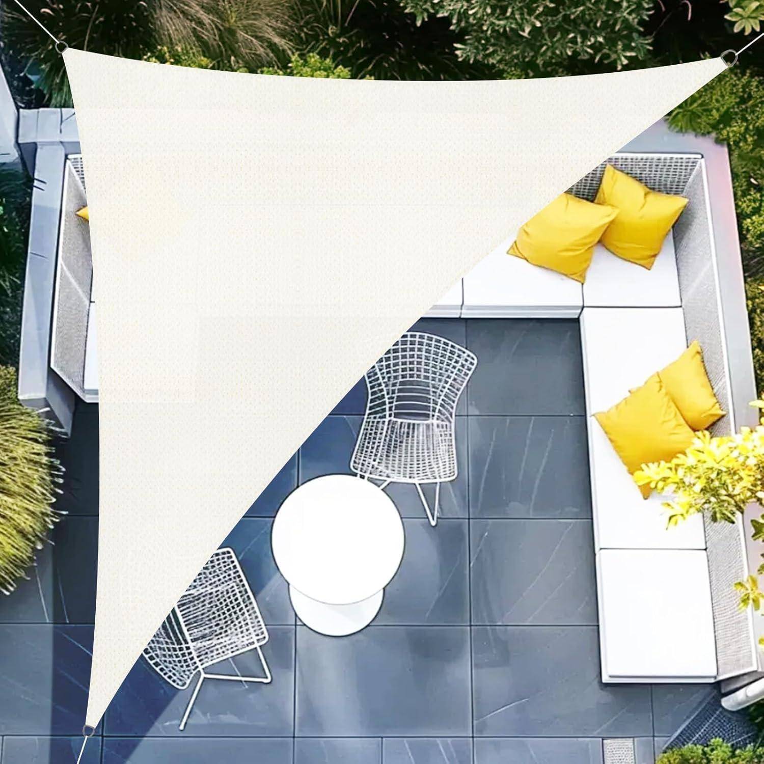 Luftaufnahme einer modernen Terrasse mit einem dreieckigen Sonnensegel über weißen Sitzmöbeln, gelben Kissen, zwei Stühlen und einem runden Tisch. Umgeben von Grünpflanzen.