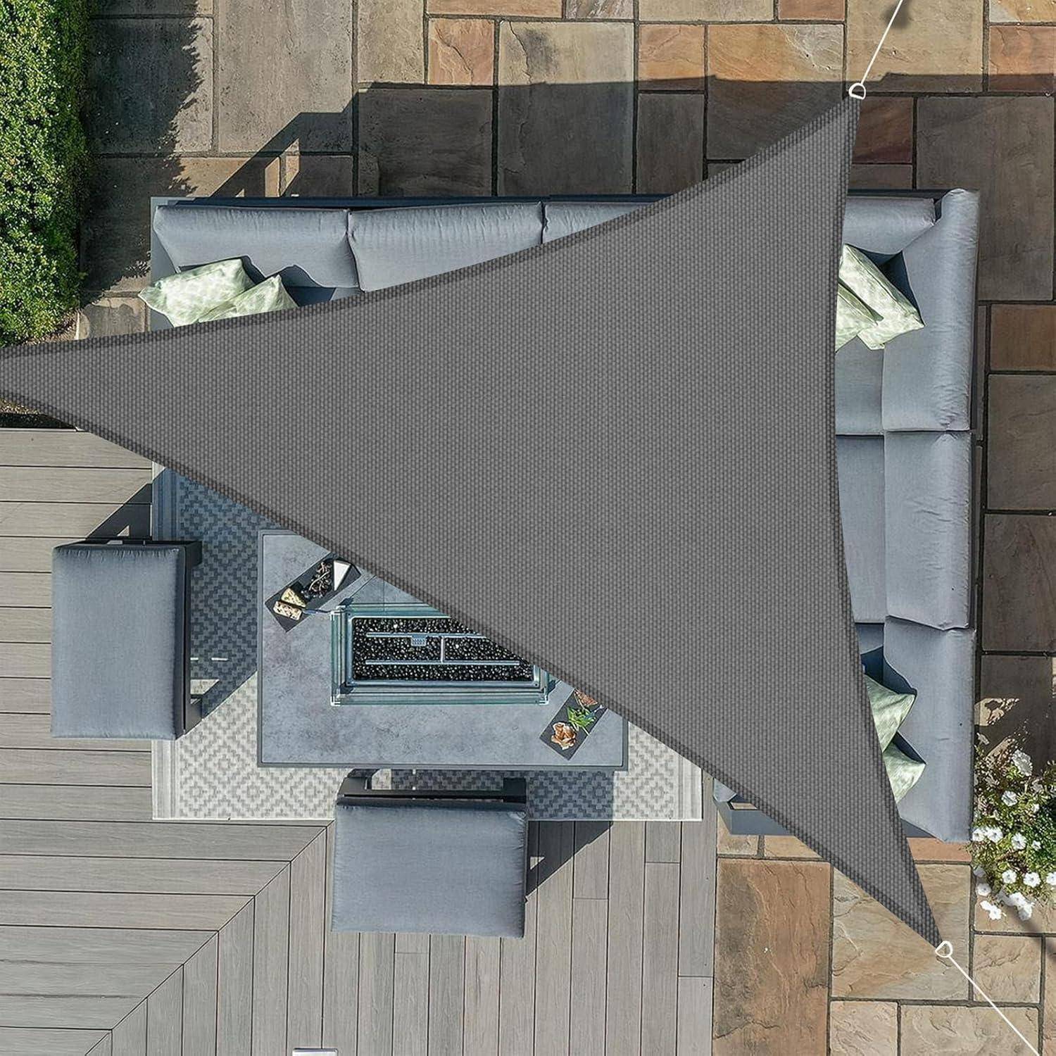 Luftaufnahme einer Terrasse mit einem dreieckigen Sonnensegel. Graue Sitzgelegenheiten umgeben eine rechteckige Feuerstelle auf einem gemusterten Teppich, mit Pflanzen in der Nähe.