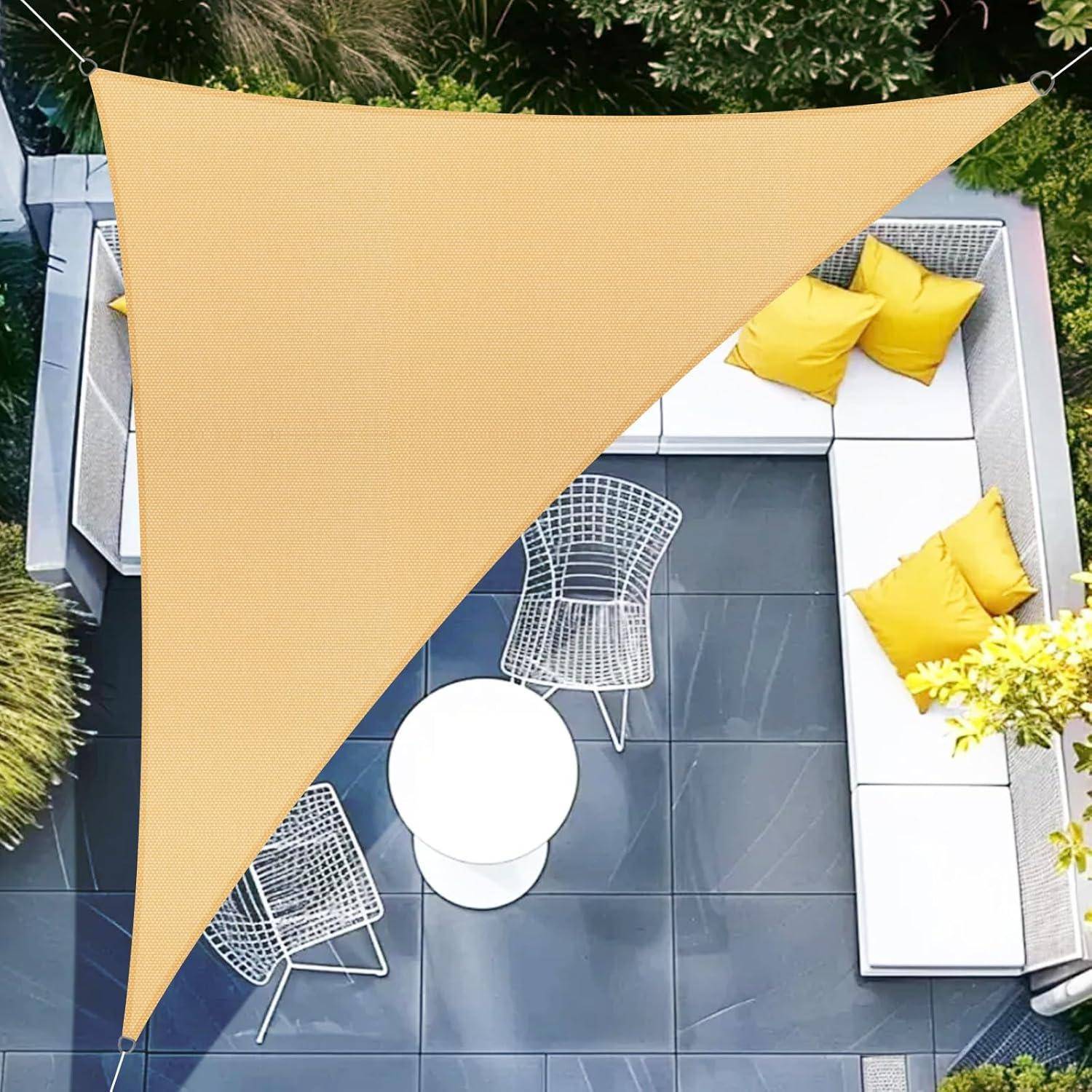 Eine Terrassensitzecke mit weißen und grauen Möbeln und gelben Kissen wird von einem dreieckigen beigen Sonnensegel beschattet. Umgebende grüne Pflanzen tragen zur ruhigen Outdoor-Atmosphäre bei.