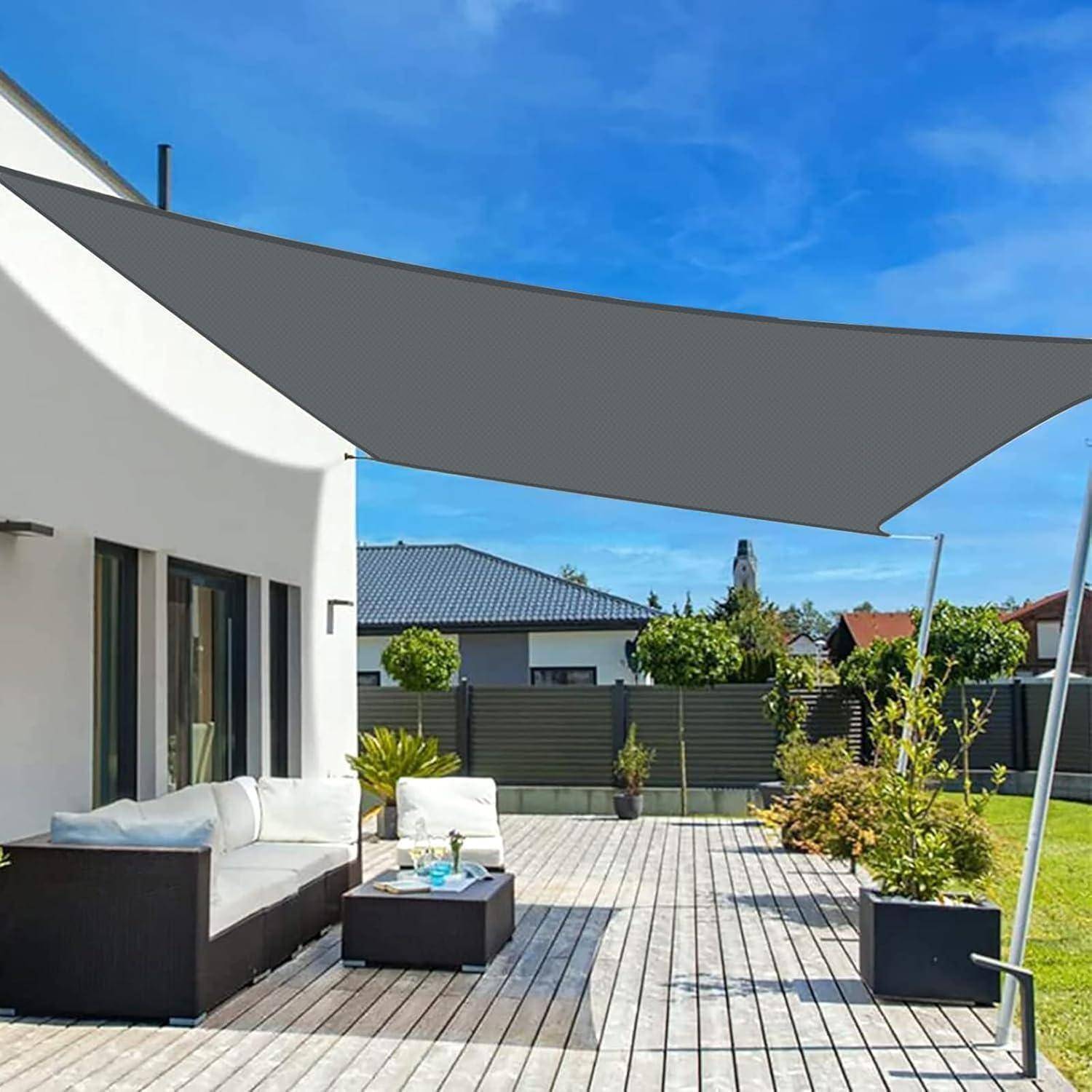 Moderne Terrasse mit einer großen Sonnensegel, einem Rattansofa und Kübelpflanzen auf einer Holzterrasse. Häuser und Bäume befinden sich im Hintergrund.