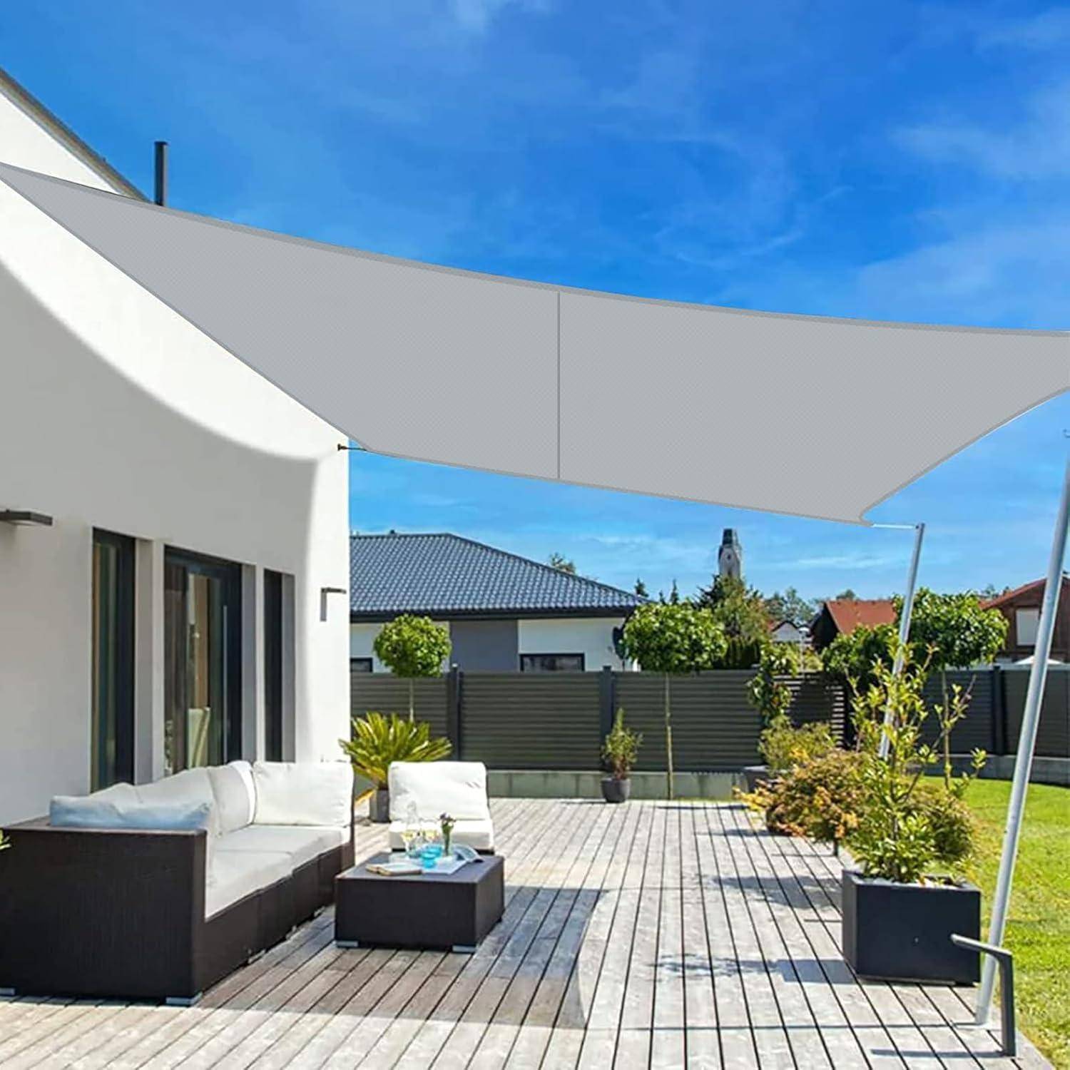 Eine moderne Terrasse mit einer Holzterrasse bietet einen grauen Sonnensegel, Outdoor-Sitzgelegenheiten, einen kleinen Tisch und Topfpflanzen unter einem klaren Himmel.