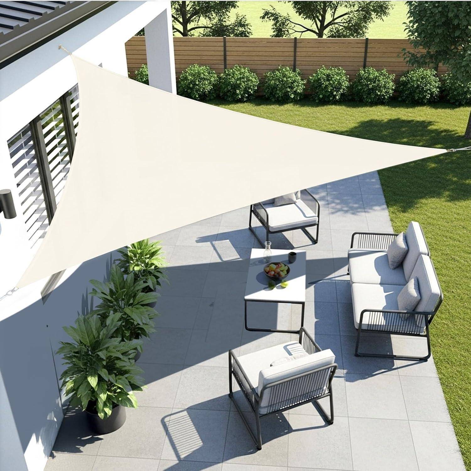 Eine moderne Terrasse mit einem dreieckigen, cremefarbenen Sonnensegel über dem Kopf, ausgestattet mit einer grauen Outdoor-Sofagruppe und einer grünen Pflanze auf einem gefliesten Boden.
