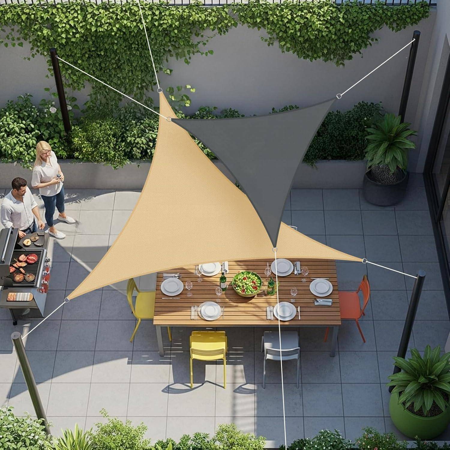 Zwei Personen grillen Essen auf einer Terrasse, wobei ein Tisch für acht Personen gedeckt ist. Bunte Stühle umgeben den Tisch unter dreieckigen Sonnensegeln.