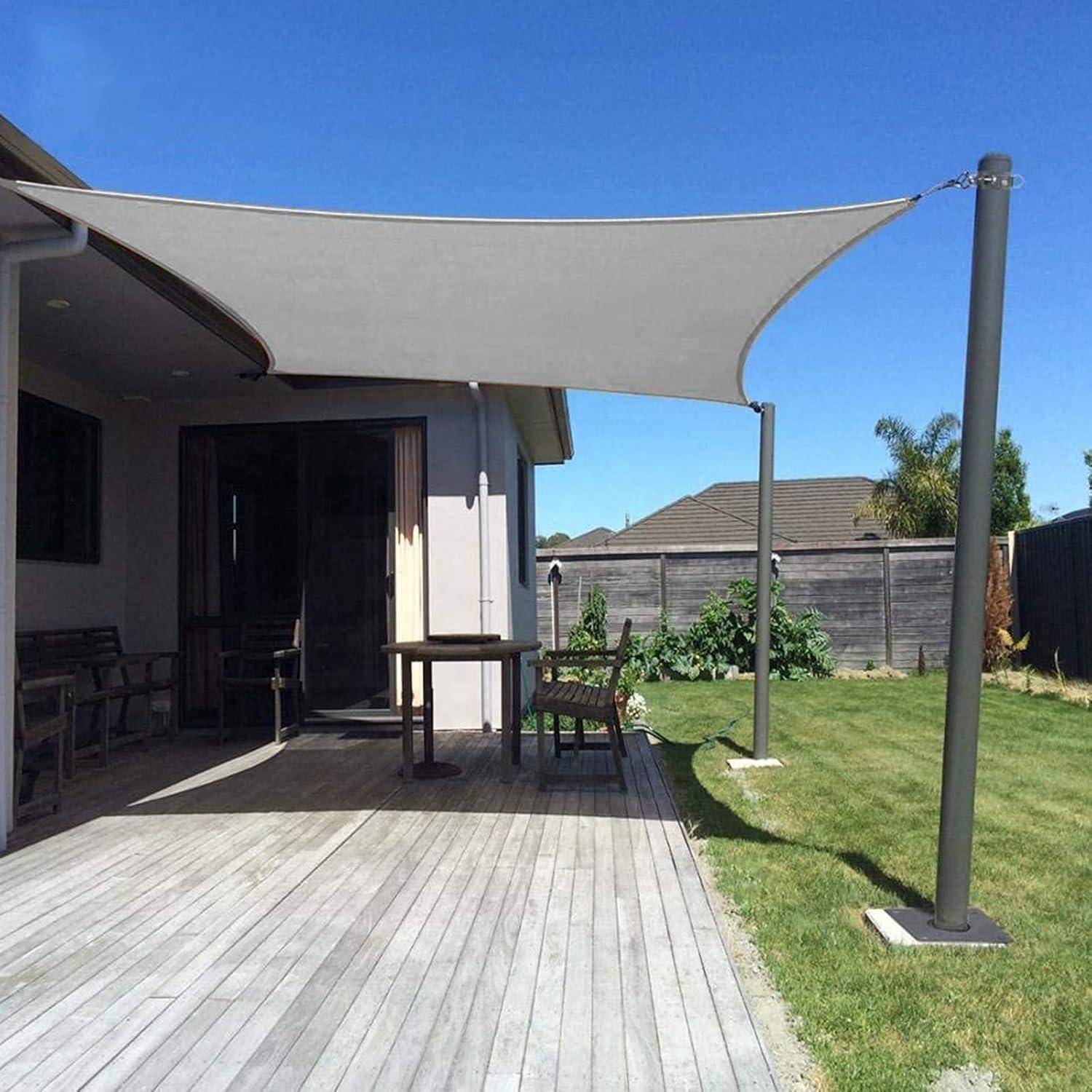 Ein Hinterhof mit einer Terrasse und Gartenmöbeln unter einem dreieckigen Sonnensegel, das an einem Haus und einem Pfahl befestigt ist und Sonnenschutz bietet.