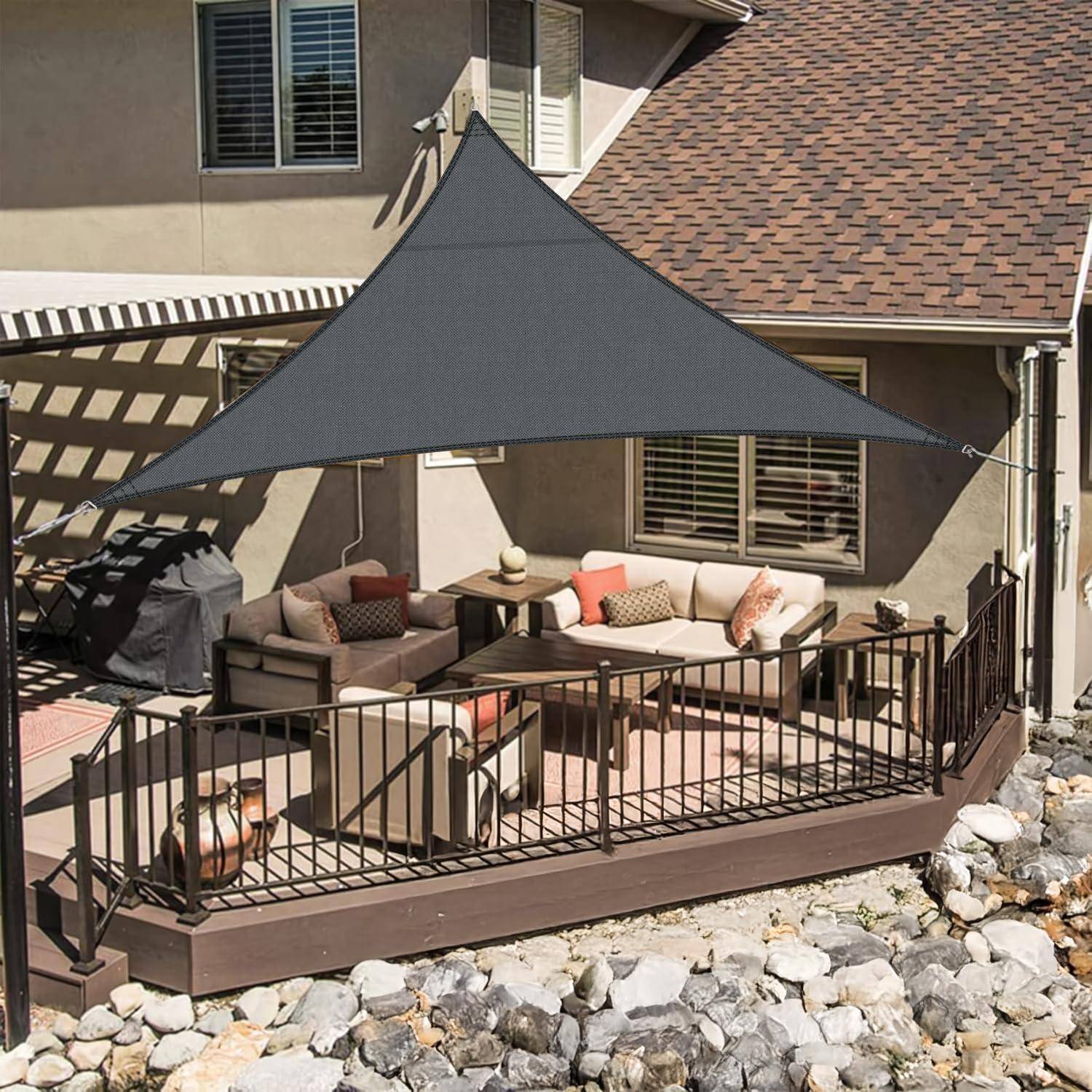 Eine moderne Terrasse mit einem grauen Sonnensegel über einer Sitzgelegenheit. Die Terrasse verfügt über gepolsterte Stühle, einen Couchtisch und dekorative Pflanzen.