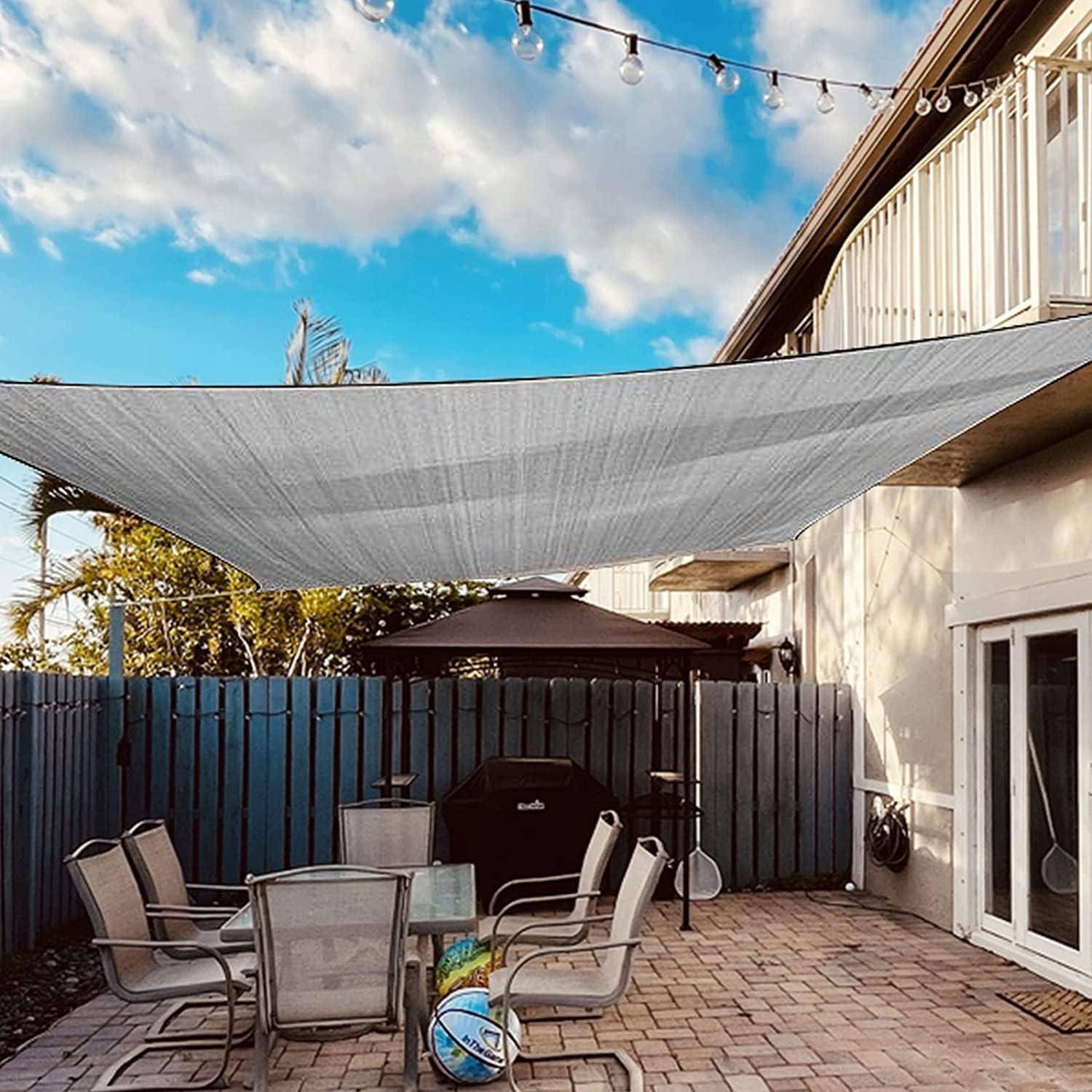 Terrasse mit einem grauen Sonnensegel über dem Kopf, Outdoor-Möbeln und einem Barbecue-Grill. Zaun und Lichterketten im Hintergrund unter einem klaren Himmel.