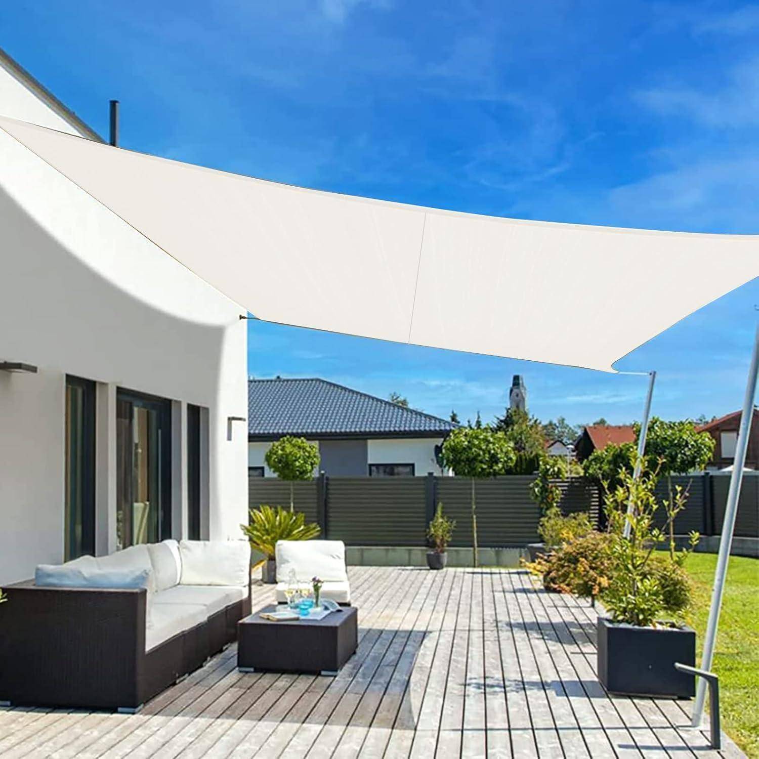 Eine moderne Terrasse mit weißem Sonnensegel, Holzterrasse, Outdoorsofa und zwei Kübelpflanzen, die einen entspannenden Außenbereich andeuten.