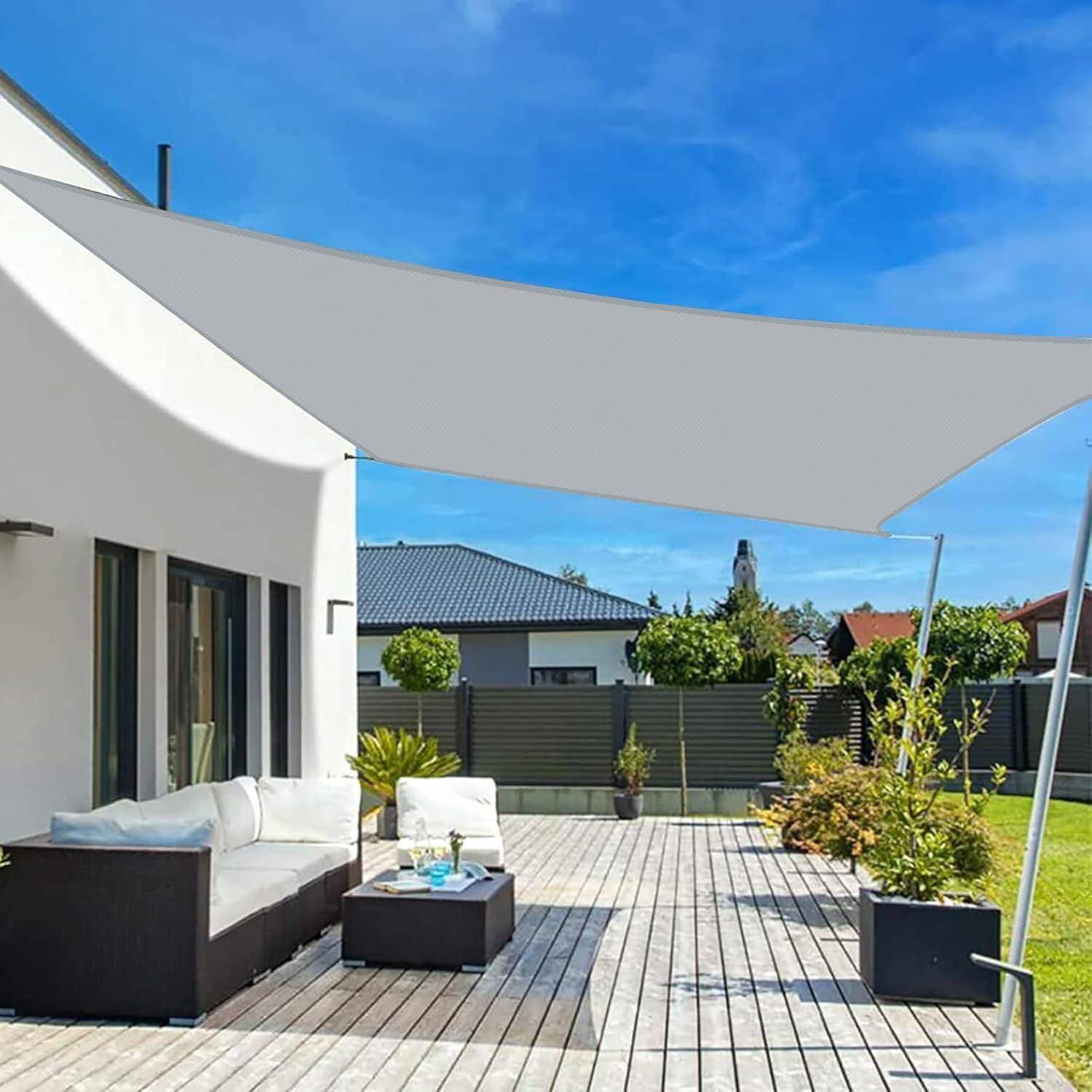 Außenterrasse mit einem modernen Sofa, Tisch und Sonnenschutz. Umgeben von Grünpflanzen und Nachbarhäusern im Hintergrund unter einem klaren Himmel.