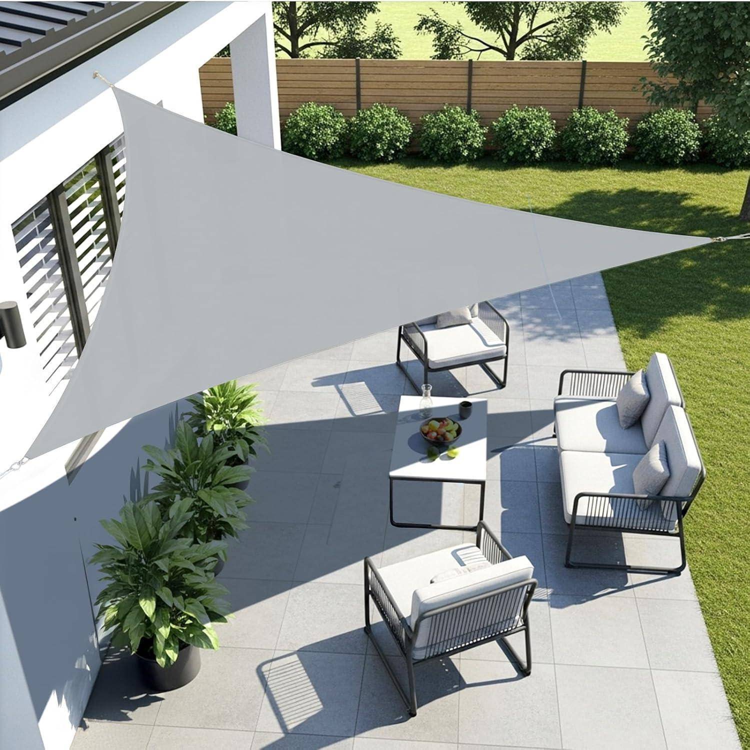 Überdachte Terrasse mit grauem Sonnensegel und moderner Sitzecke, einschließlich Sofa, Stühlen und Tischen auf gefliesten Böden, umgeben von Grünpflanzen.
