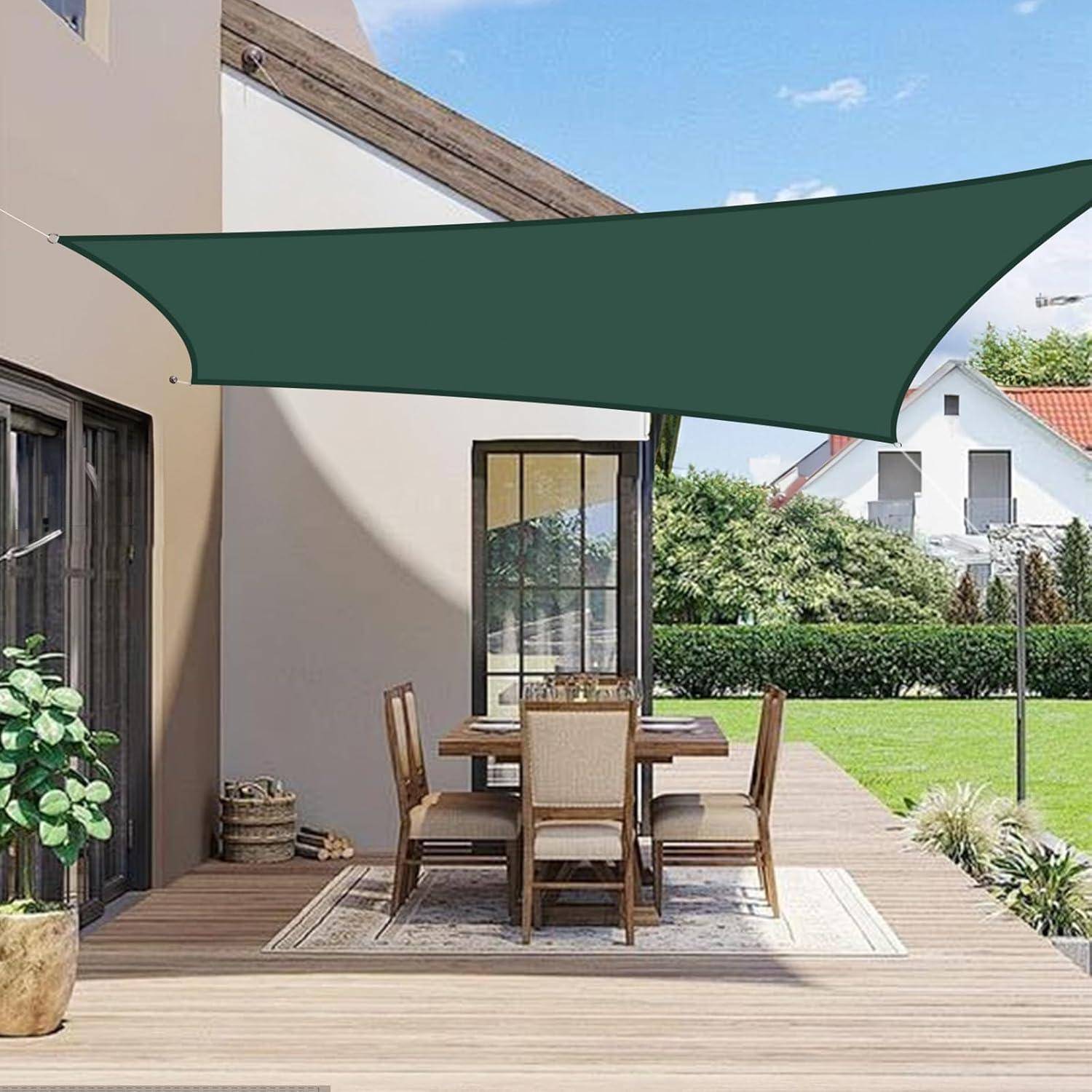 Sitzbereich im Freien auf einer Holzterrasse mit Tisch, Stühlen und grünem Sonnenschirm über dem Sitzplatz. Haus und Rasen mit Hecken im Hintergrund.