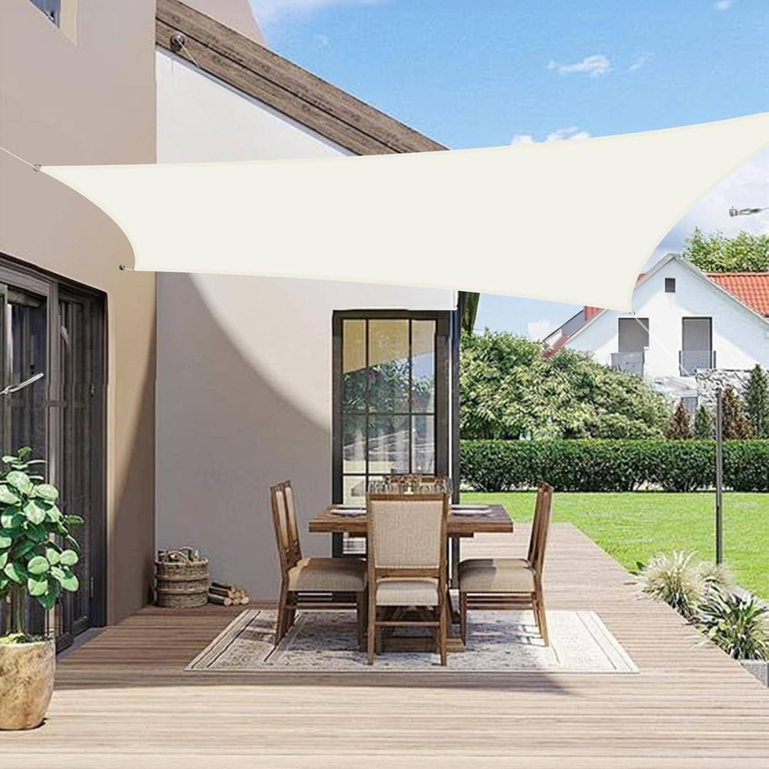 Terrassenbereich im Freien mit einem Esstisch und Stühlen unter einem weißen dreieckigen Sonnensegel. Ein Haus und ein Garten sind im Hintergrund sichtbar.