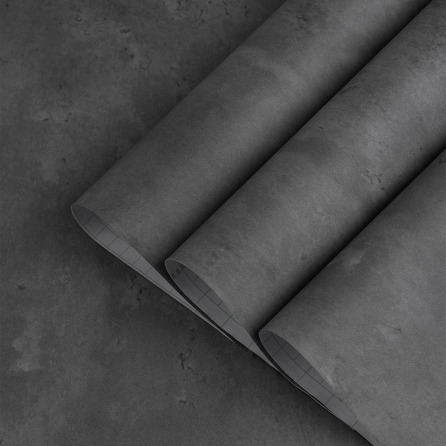 Drei Rollen graues Tapetenmaterial auf einer ähnlich grauen Oberfläche, die ein strukturiertes Muster auf dem Material zeigen.