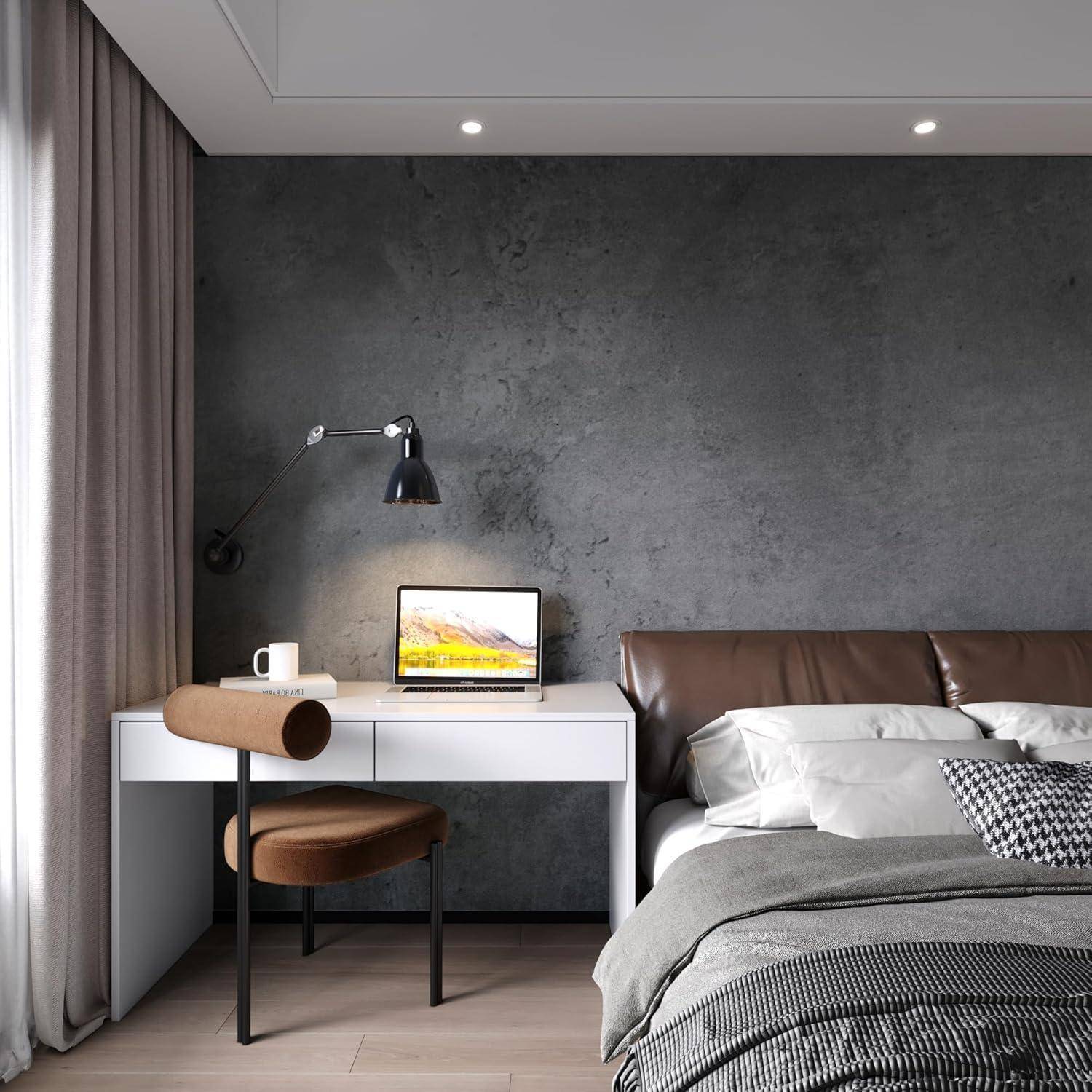 Ein modernes Hotelzimmer verfügt über ein ordentlich gemachtes Bett, einen Schreibtisch mit einem Laptop und eine wandmontierte Lampe, die einen gemütlichen und funktionalen Arbeitsbereich schafft.
