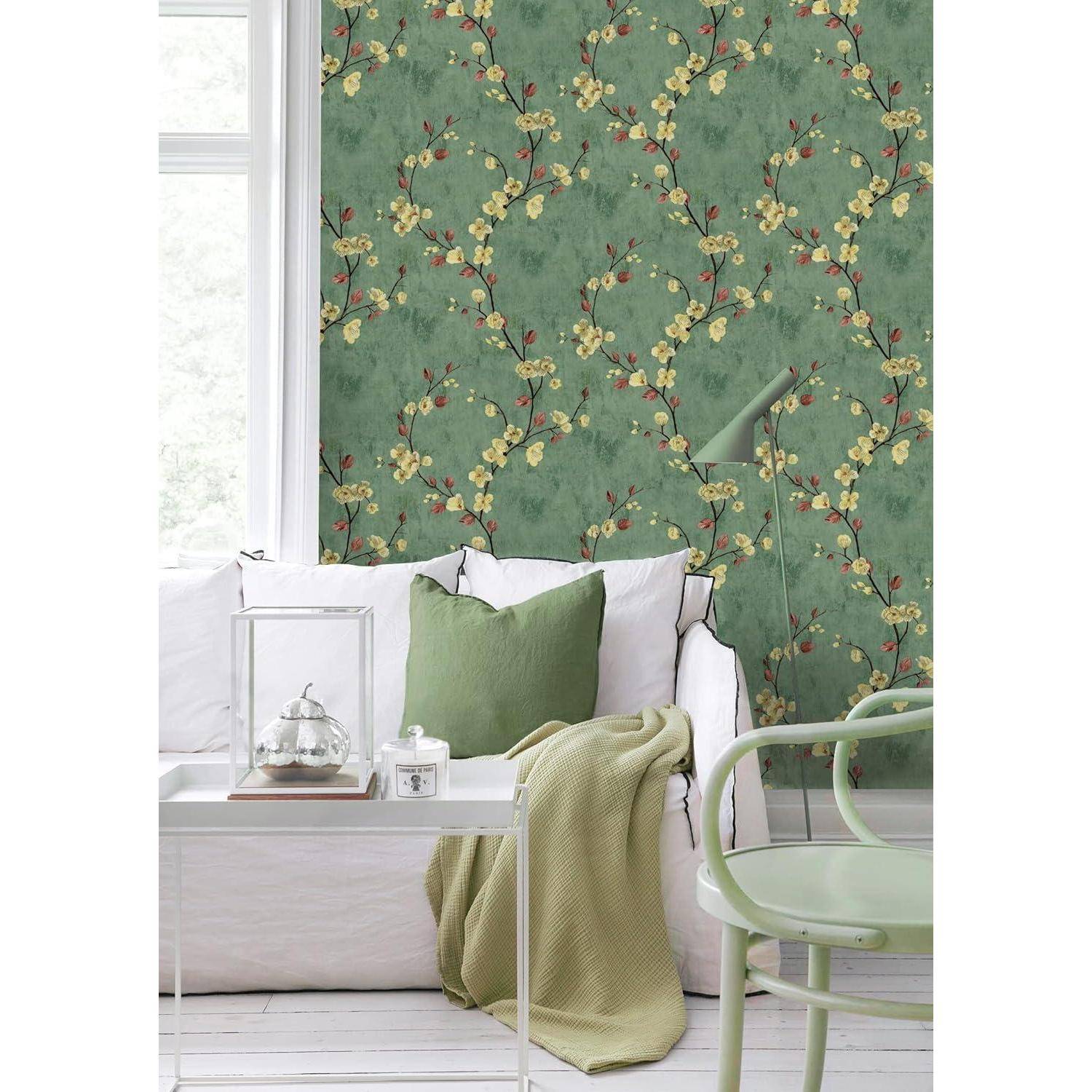 Ein gemütliches Wohnzimmer mit einem weißen Sofa, einem grünen Kissen und einem passenden Sessel vor einer grün-floralen Tapete. Eine Stehlampe steht in der Nähe.
