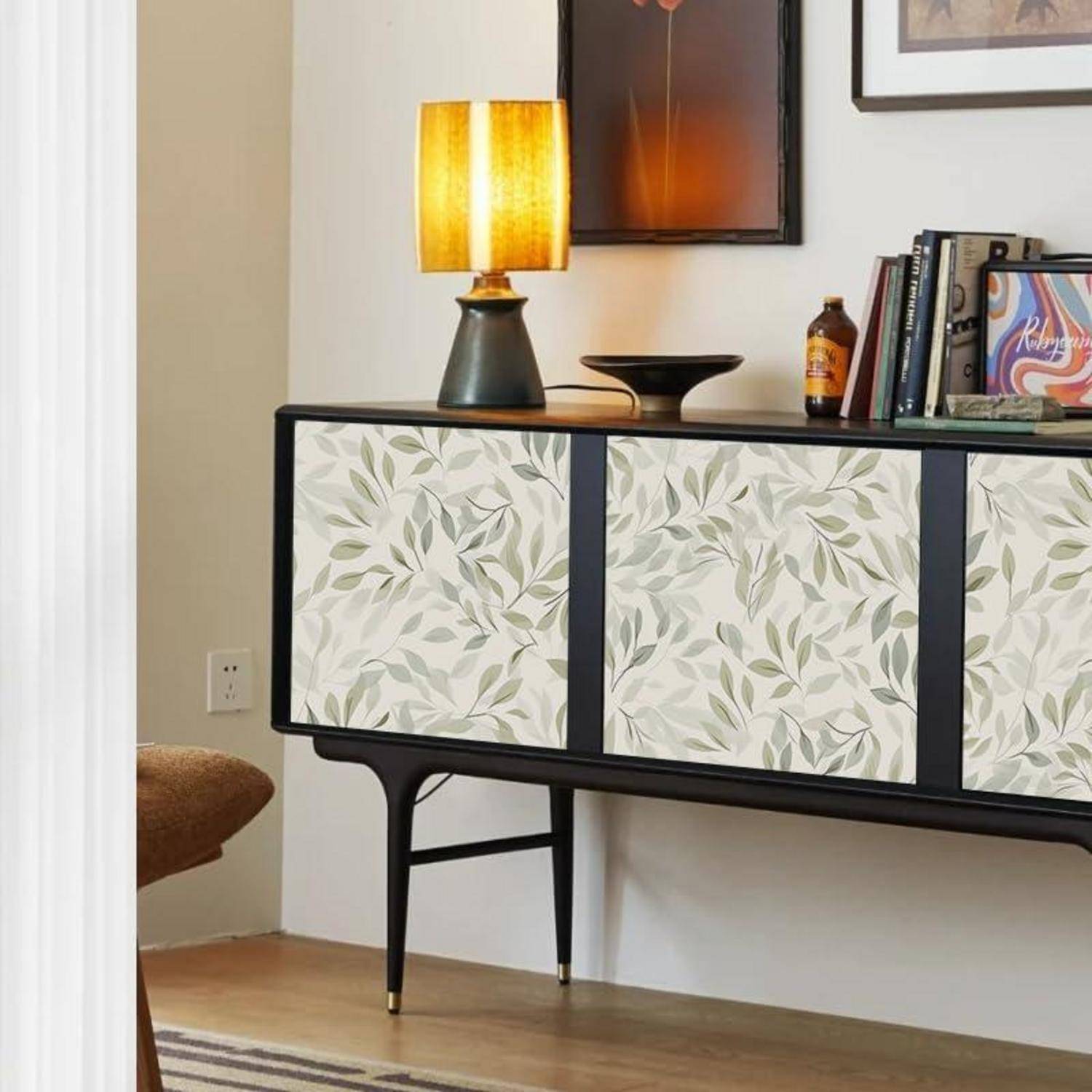 Ein Sideboard im Stil der Mitte des 20. Jahrhunderts mit einem botanischen Muster, eine Tischlampe, Bücher und ein gerahmtes Kunstwerk an der Wand schaffen eine gemütliche Ecke.