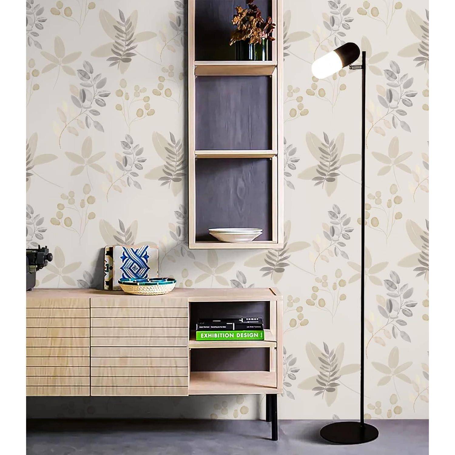 Ein moderner Wohnraum zeigt eine Stehlampe, eine gemusterte Tapete mit Blättern und ein Holzsideboard, das Bücher und Dekorationsgegenstände trägt.