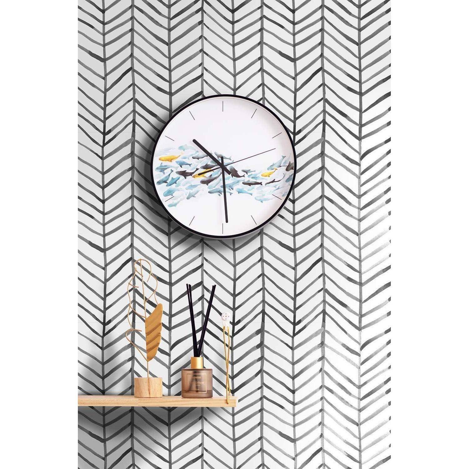 Eine runde Wanduhr mit einem Wolkenmuster, die 10:10 zeigt, hängt an einer Wand mit Fischgrätenmuster. Darunter befindet sich ein Holzregal mit dekorativen Gegenständen.